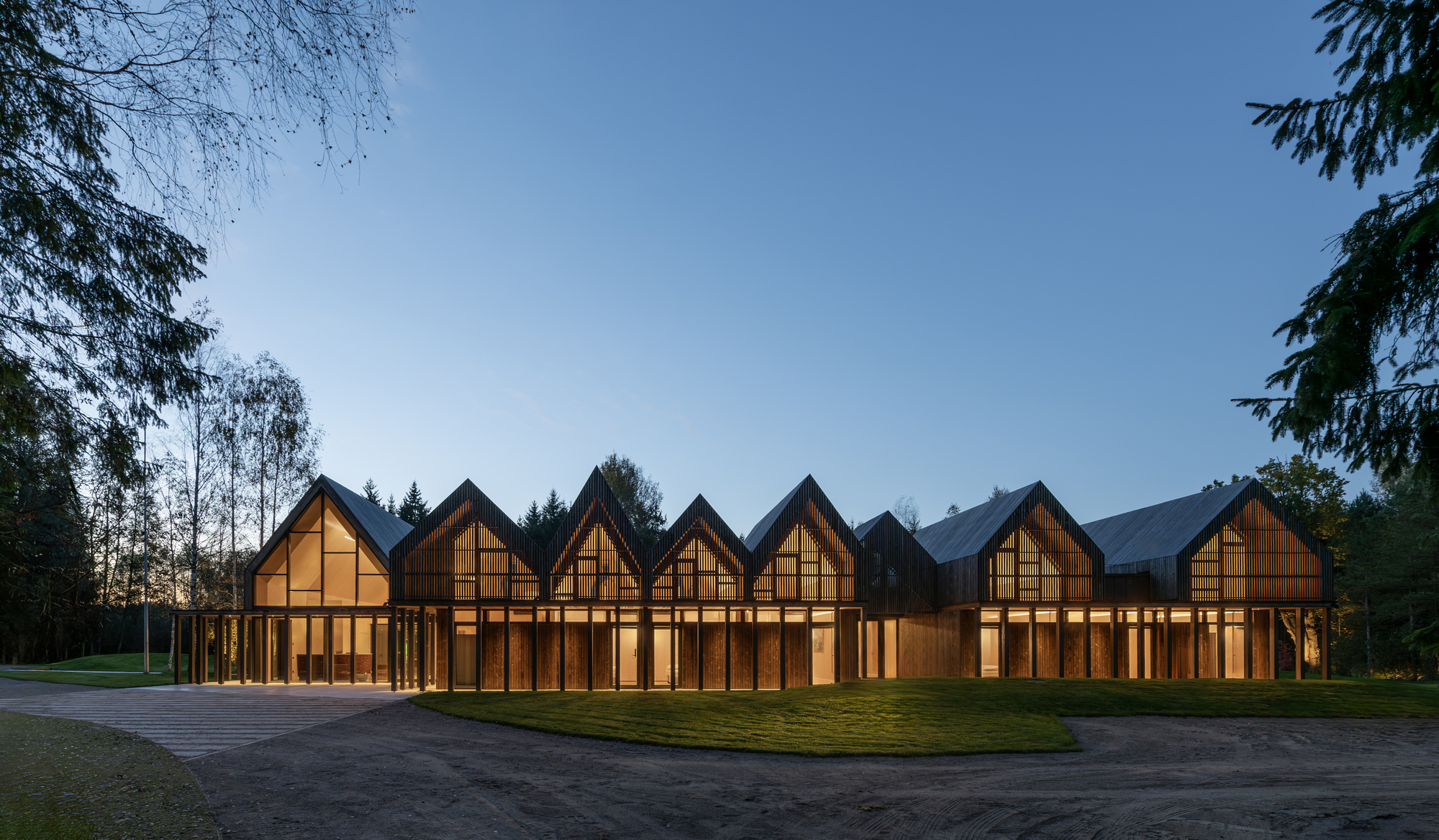 Facade with repeating triangular gabled forms framing glazed bays under timber framing at twilight
