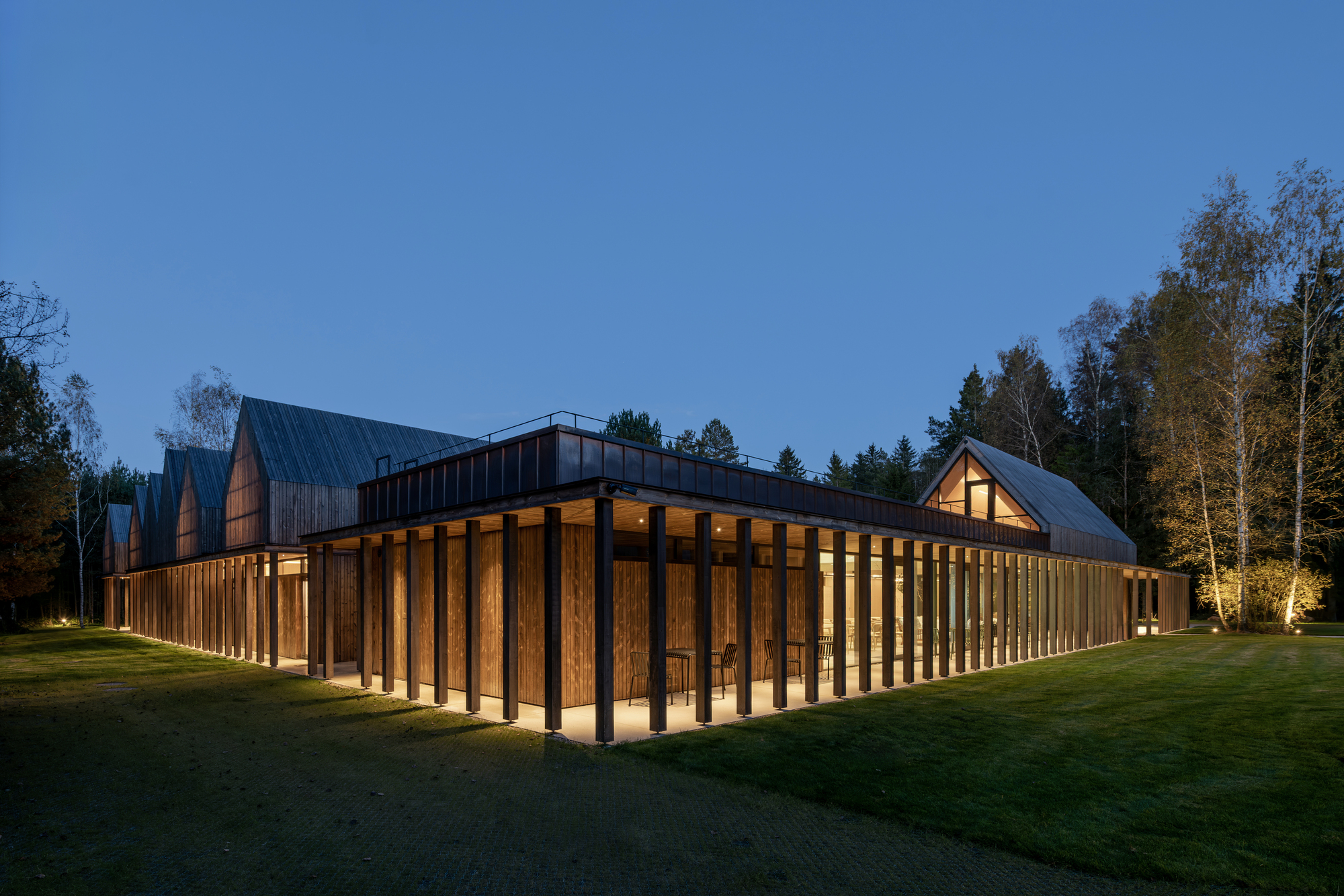 Corner view of timber colonnade wrapping the perimeter with illuminated interior spaces at night