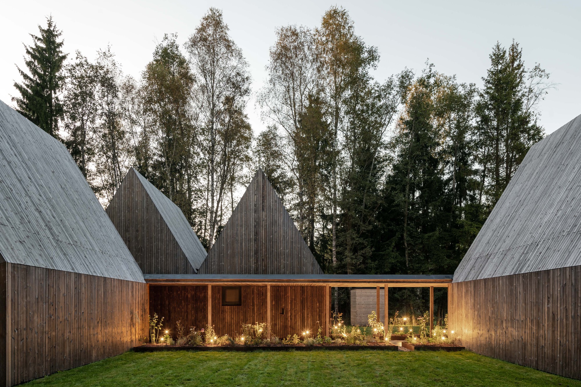 Interior courtyard framed by timber-clad gables with planted beds and uplighting at twilight