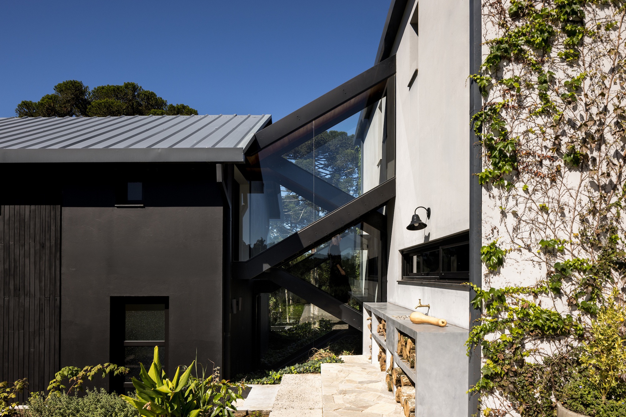 Outdoor kitchen with stone counter, timber oven and black steel pergola beneath glazed walkway
