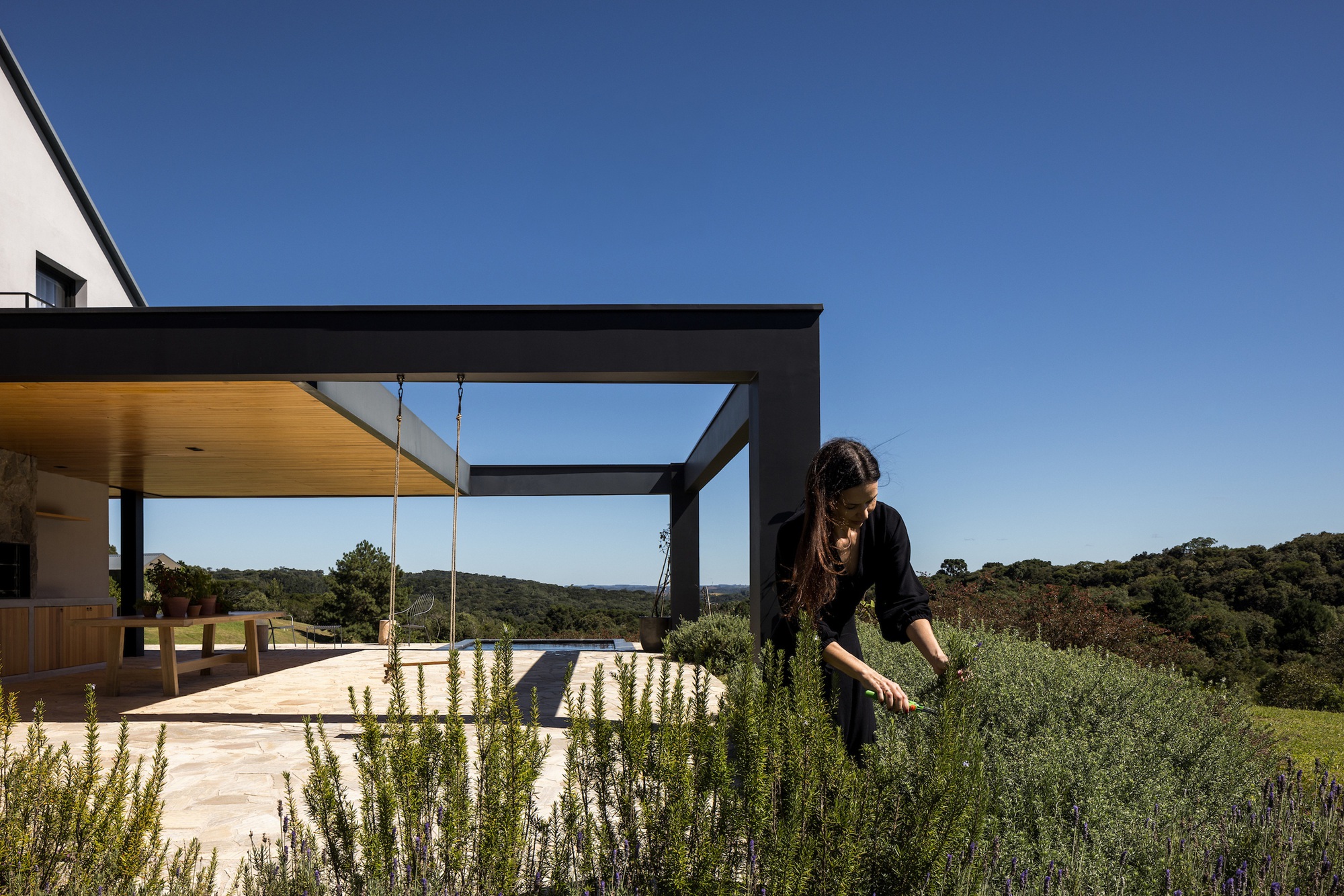 Rooftop terrace with black steel pergola, planted herbs and a figure tending the garden