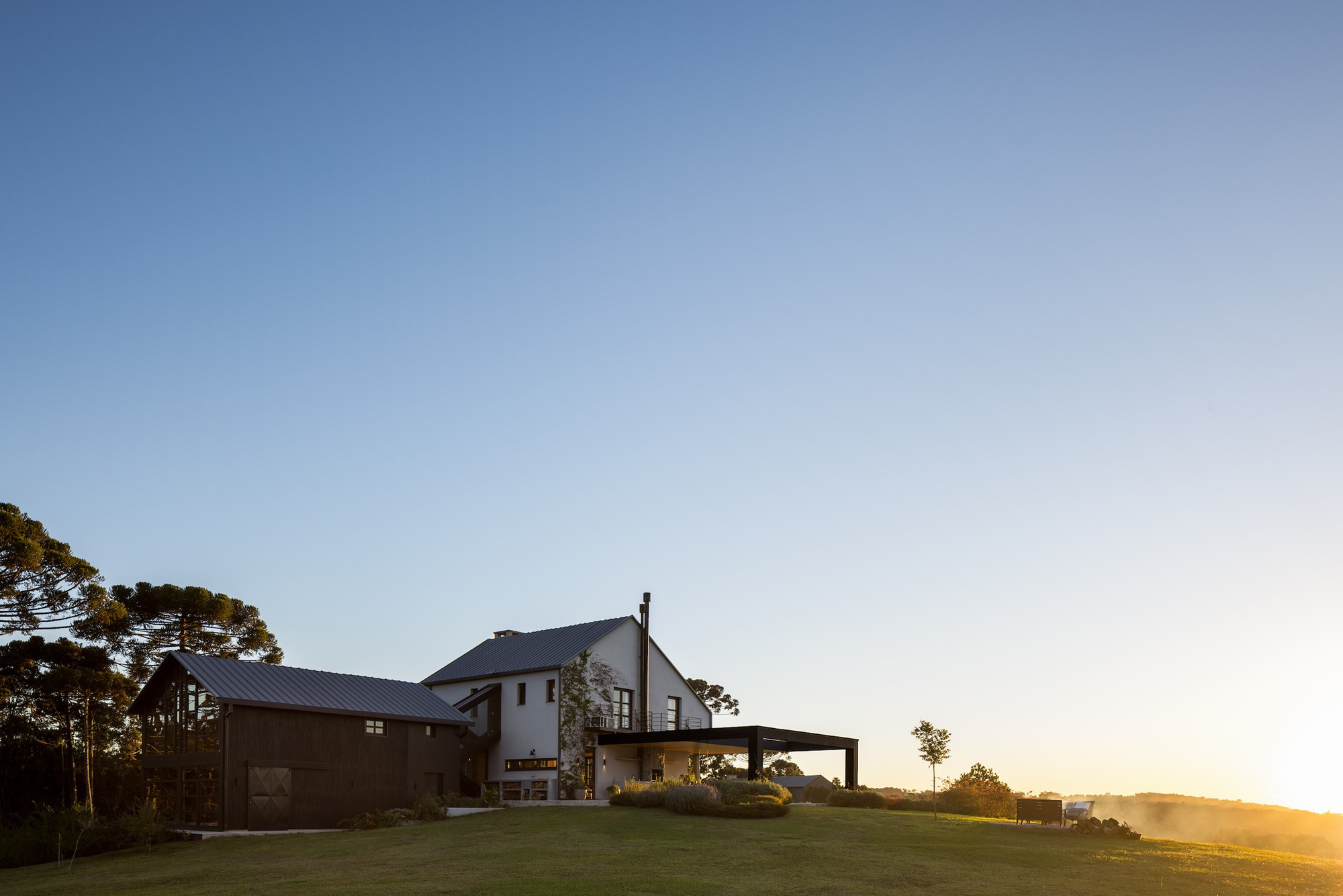 House with covered terrace and metal roofs on a lawn at sunset with golden light