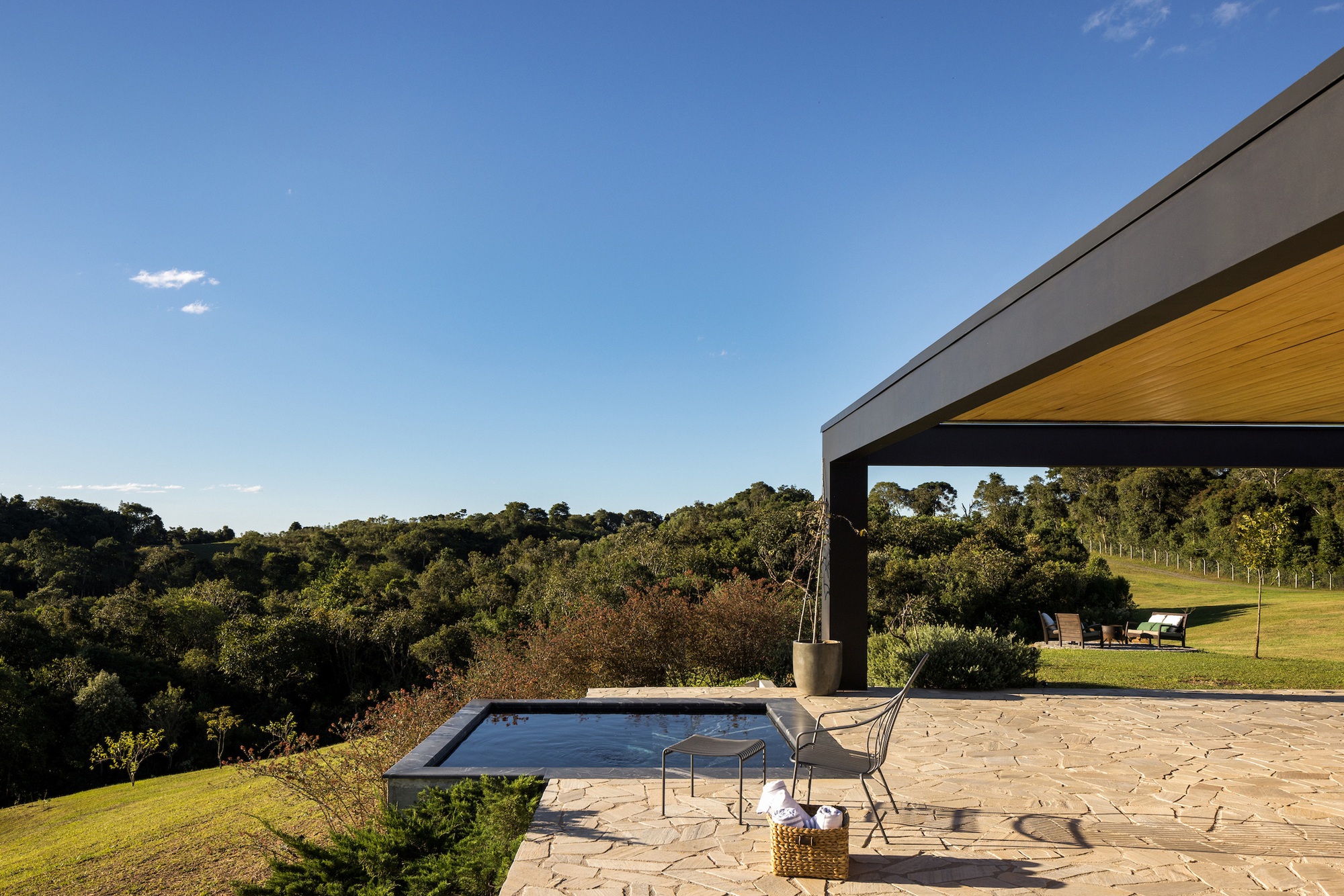 Terrace with rectangular pool and flagstone paving overlooking rolling green hills under clear sky