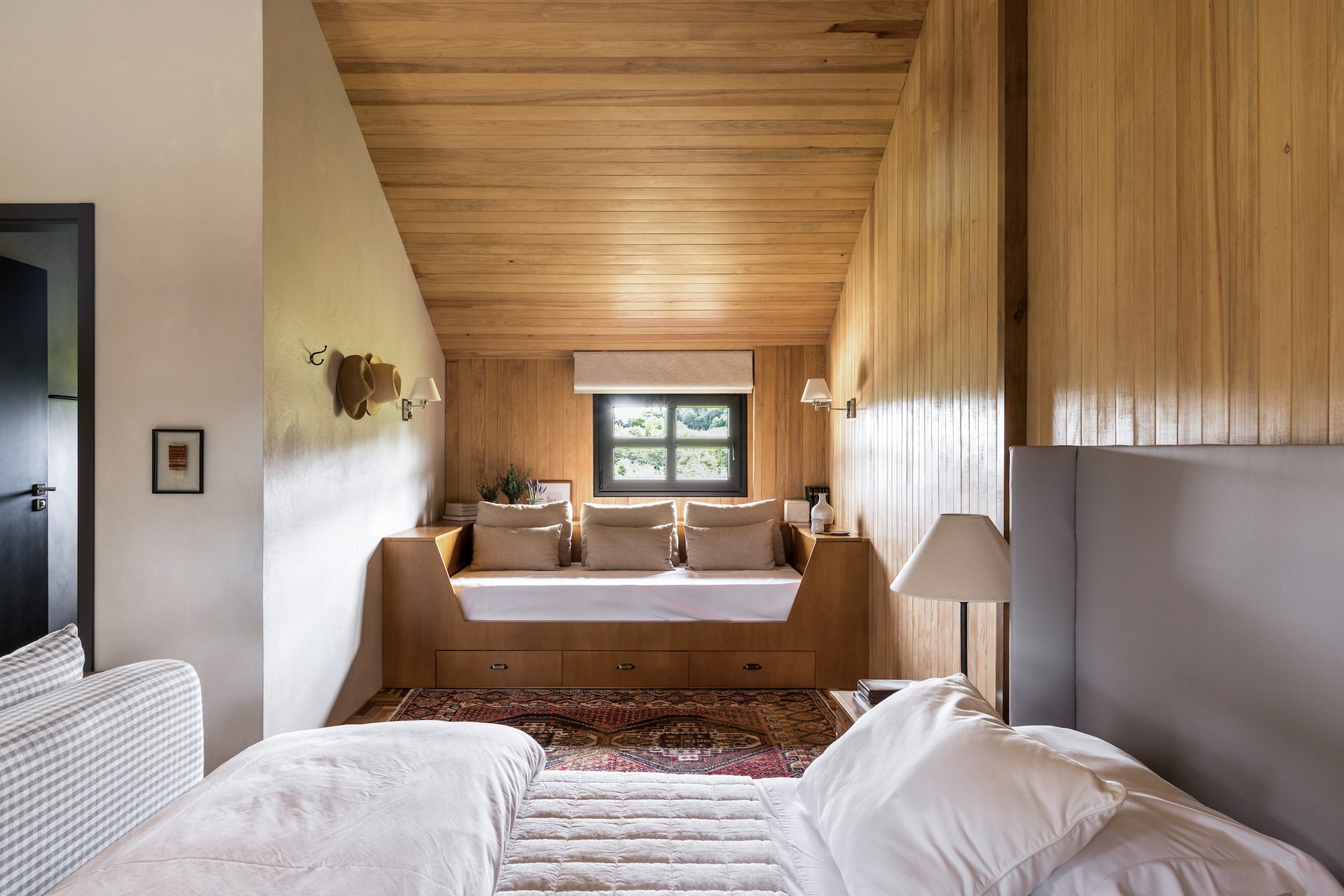 Bedroom with timber-clad ceiling and built-in window seat beneath a square picture window
