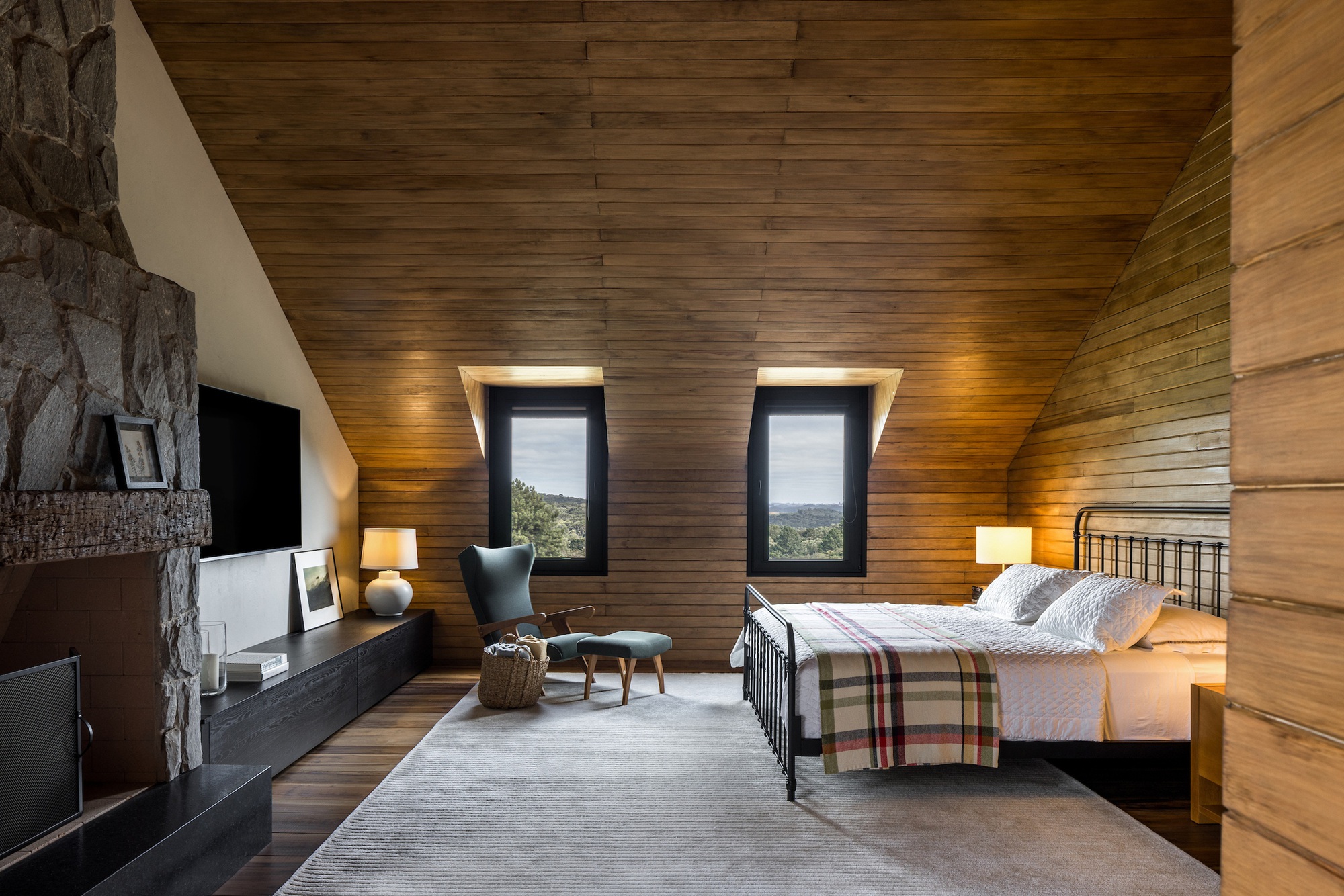 Bedroom with sloped timber-clad ceiling and two vertical windows framing distant landscape views