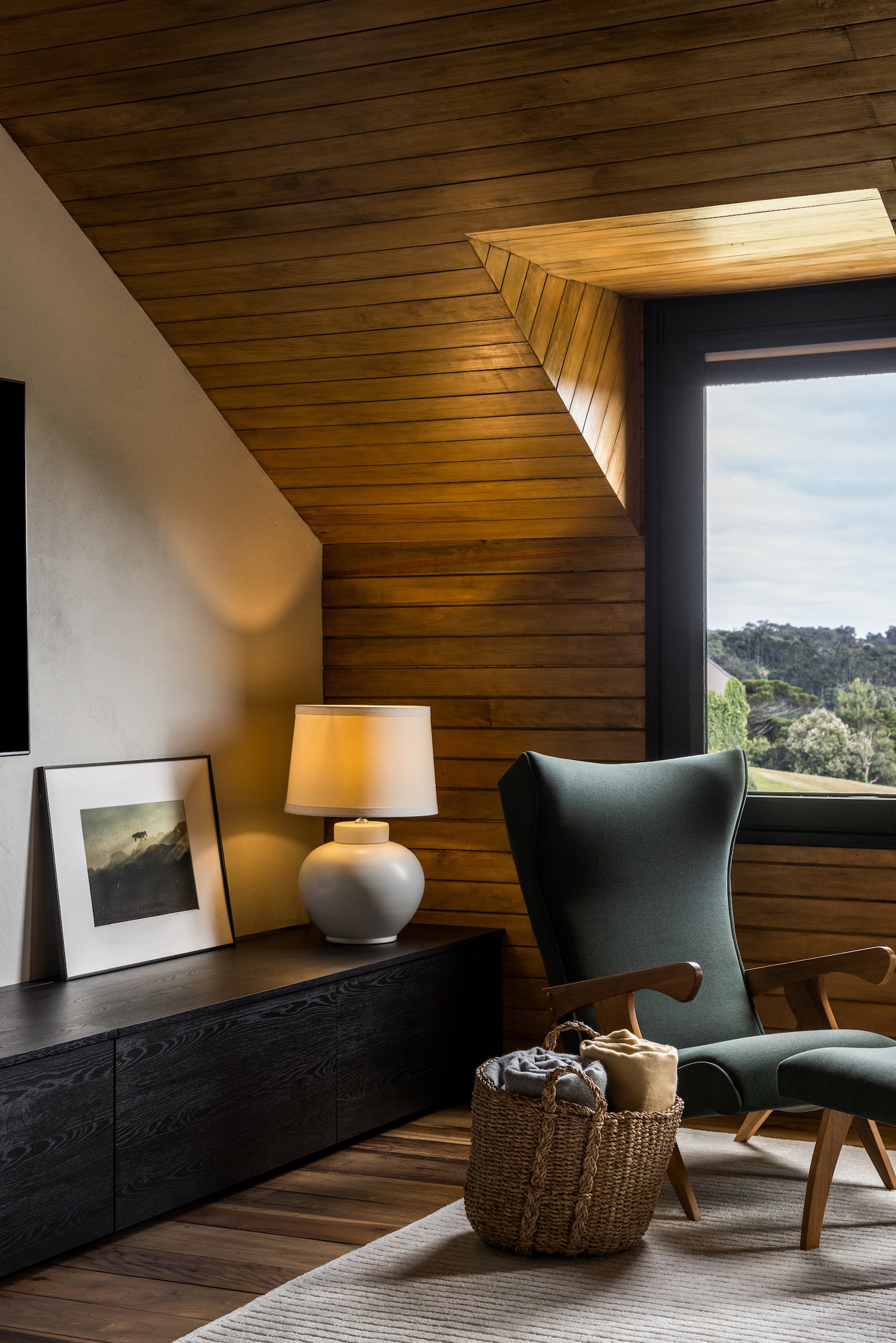 Corner seating nook with angled timber-clad walls and vertical window with afternoon sunlight