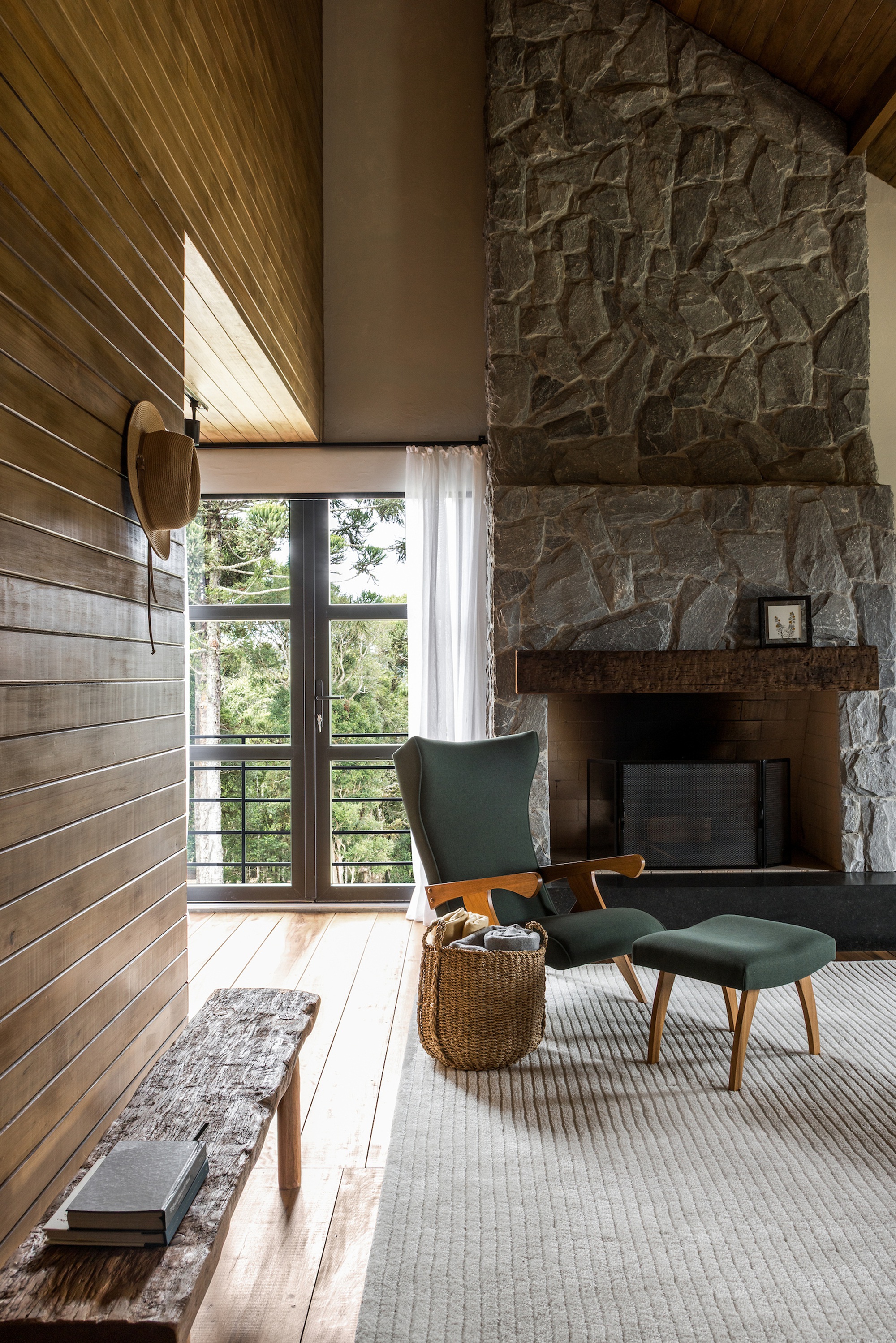 Double-height living room with stone fireplace chimney, timber plank ceiling and glazed door to greenery beyond