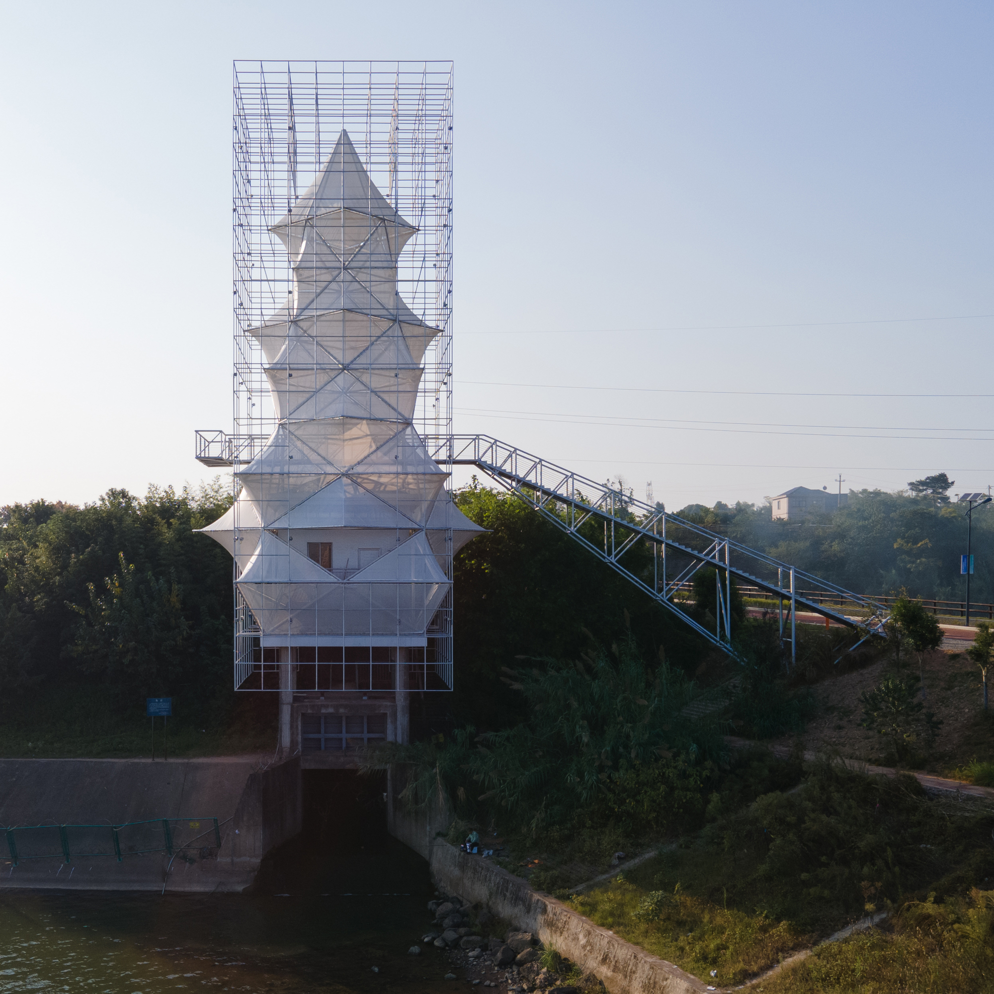 The scaffolded pagoda-like structure with its ramped bridge crossing a canal at dawn