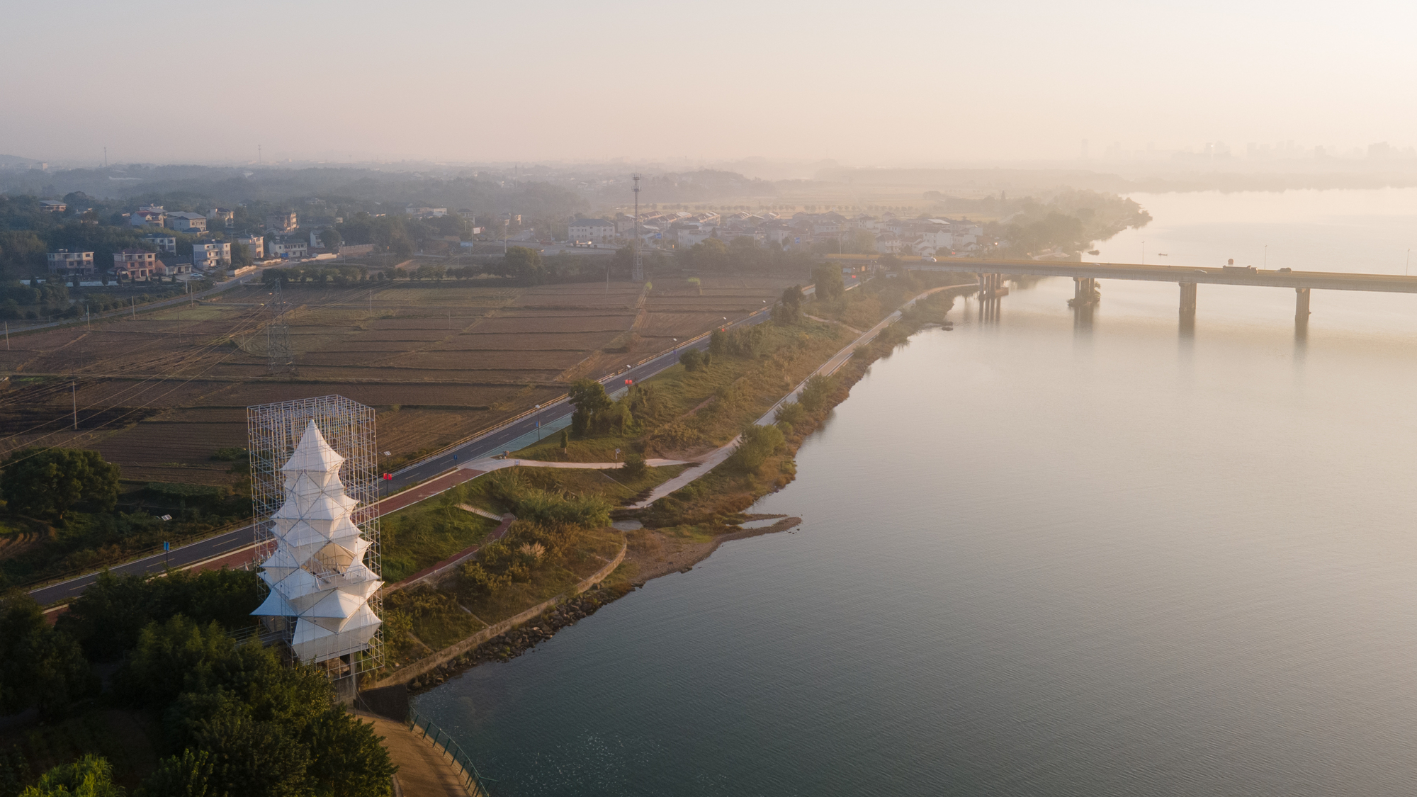 Drone view of the tower on the riverbank with fields, roadway and a bridge at sunrise