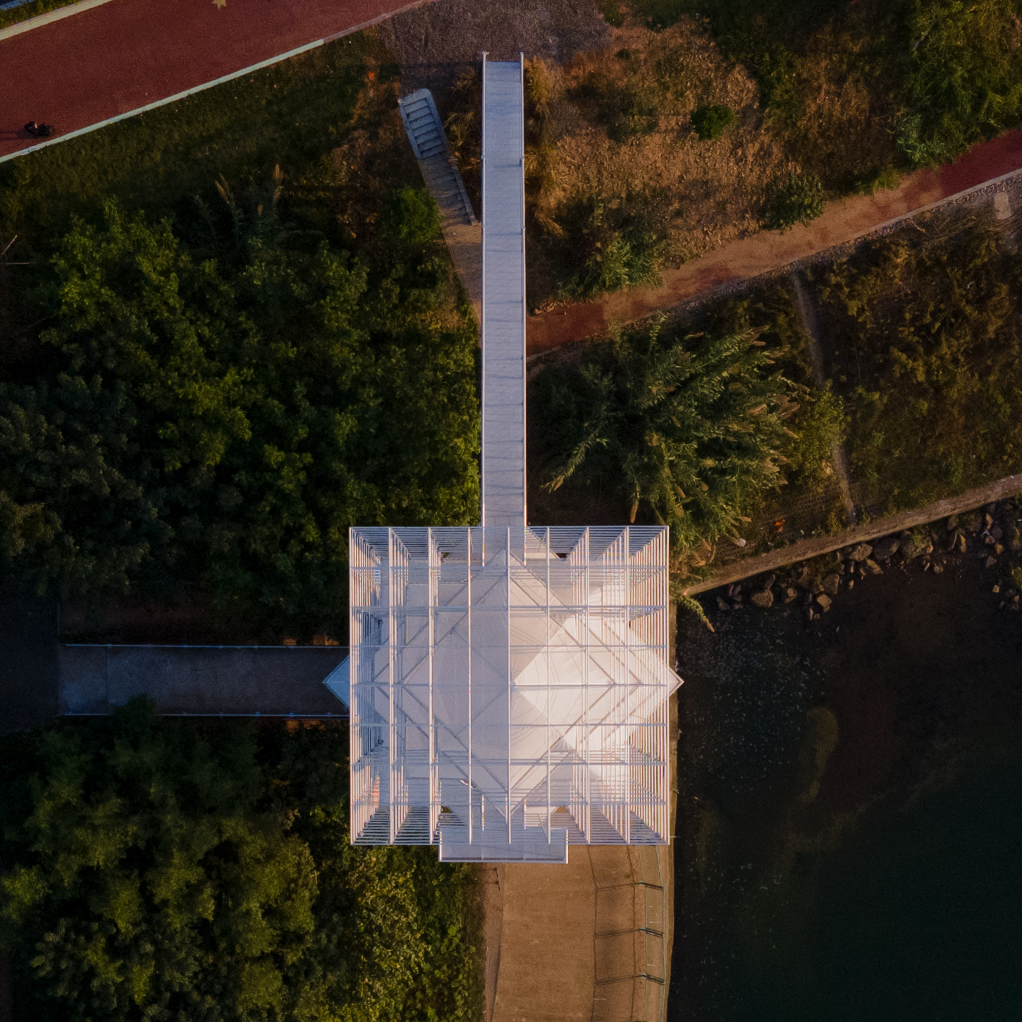 Overhead drone view of the pyramidal roof platform and metal walkway surrounded by dense trees and red pathways