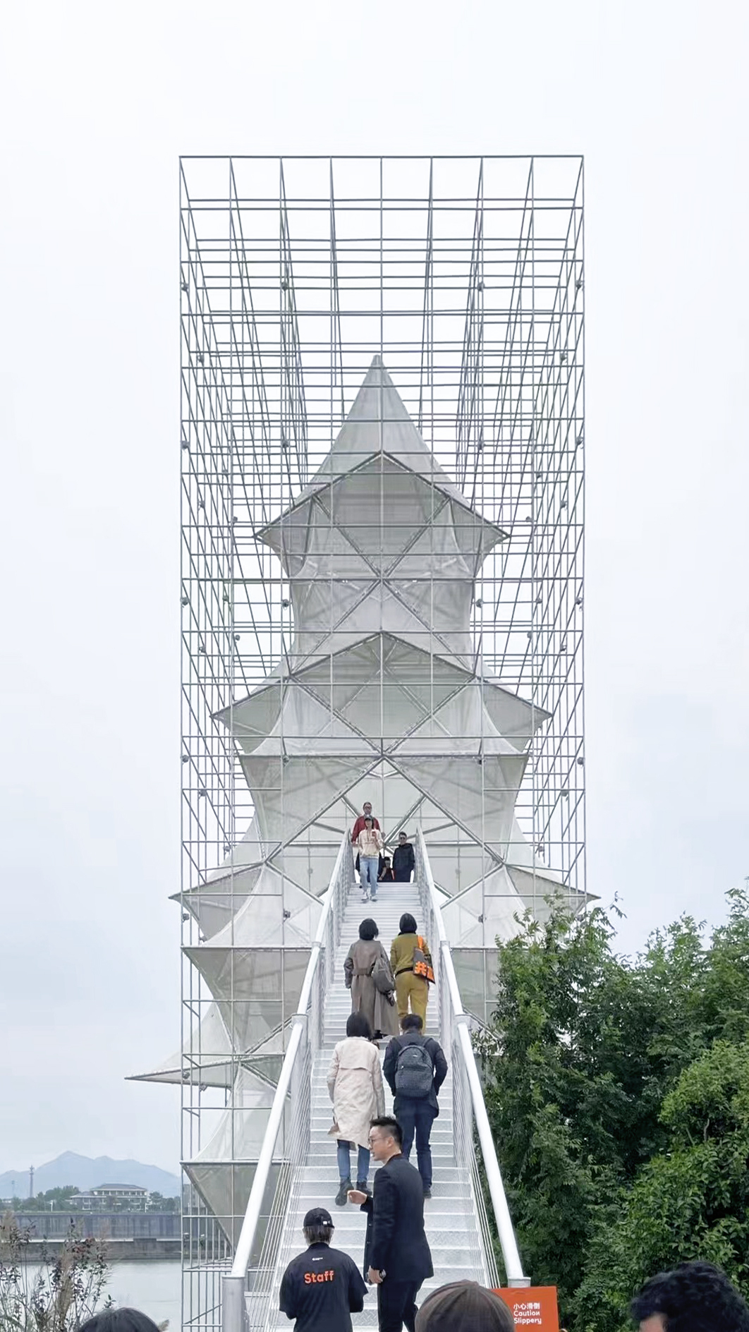 Visitors ascending the white metal stairway through the open scaffold structure on an overcast day