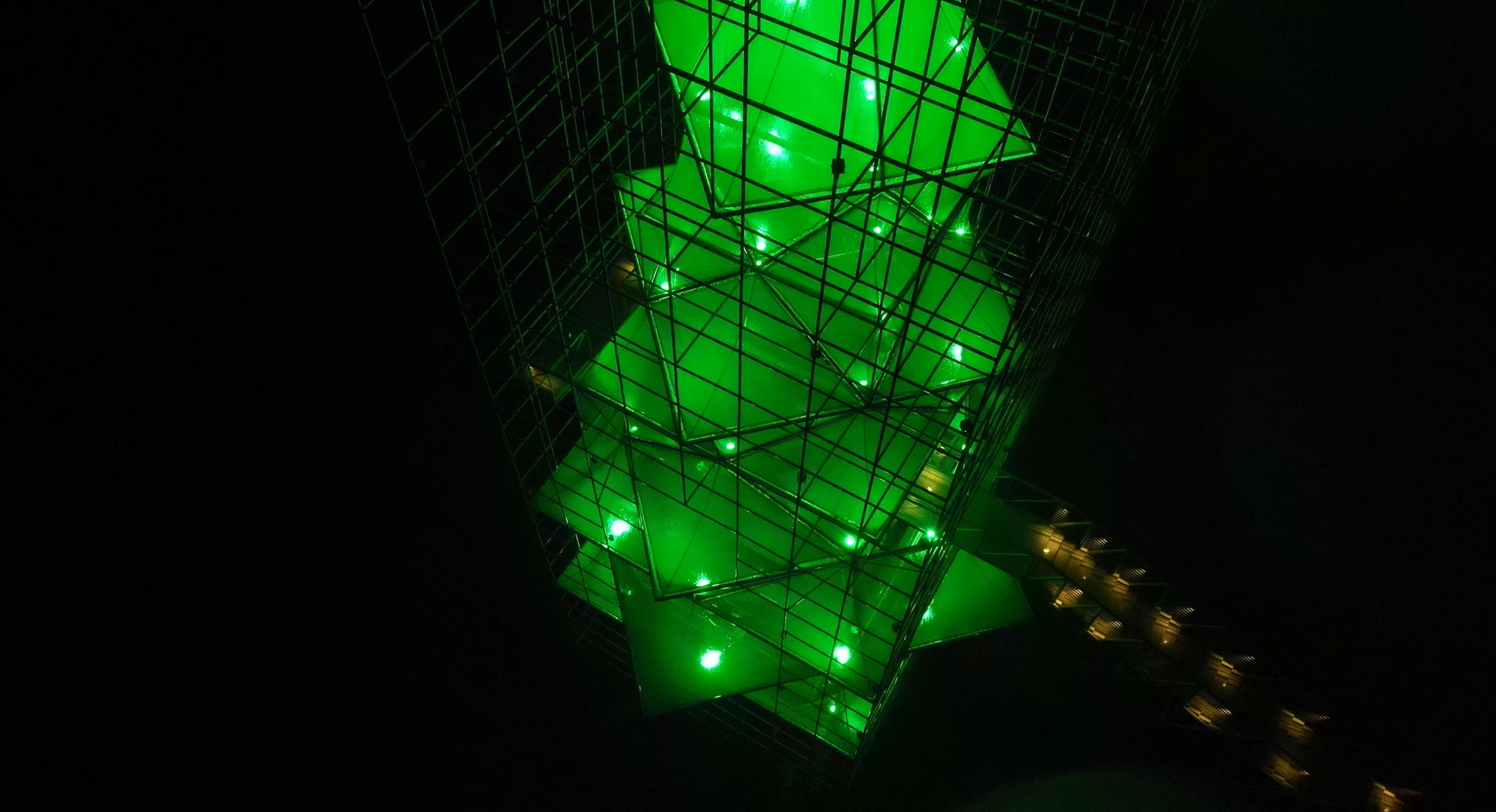 Aerial view of the illuminated pyramidal structure with green lighting glowing through the triangulated steel framework at night