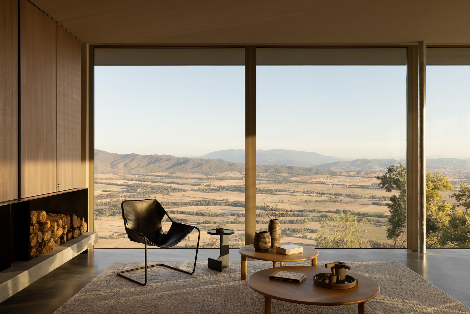 Interior living space with floor-to-ceiling glazing and fireplace overlooking the valley landscape in warm afternoon light