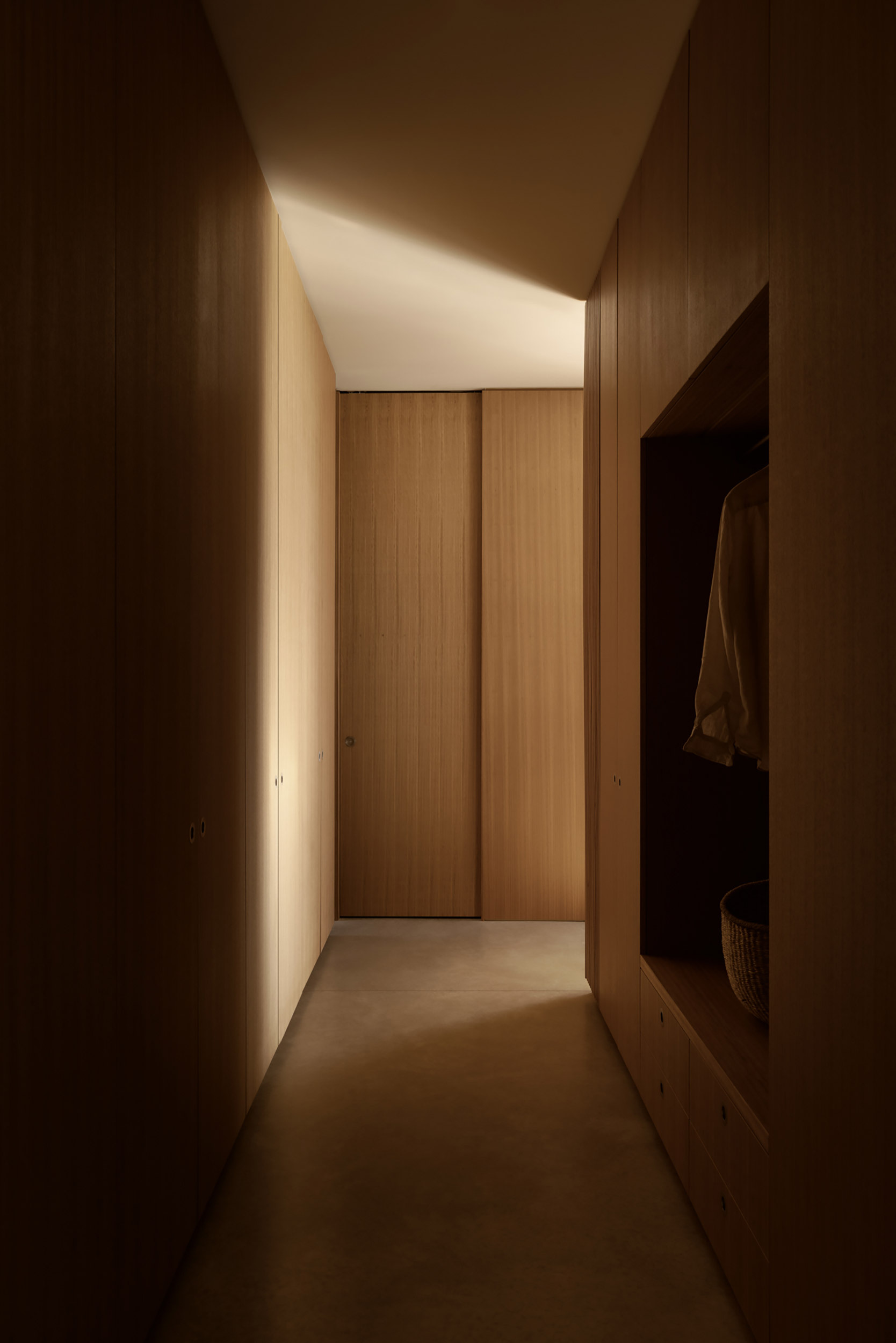 Corridor with timber-paneled walls and concealed doors illuminated by a clerestory slot