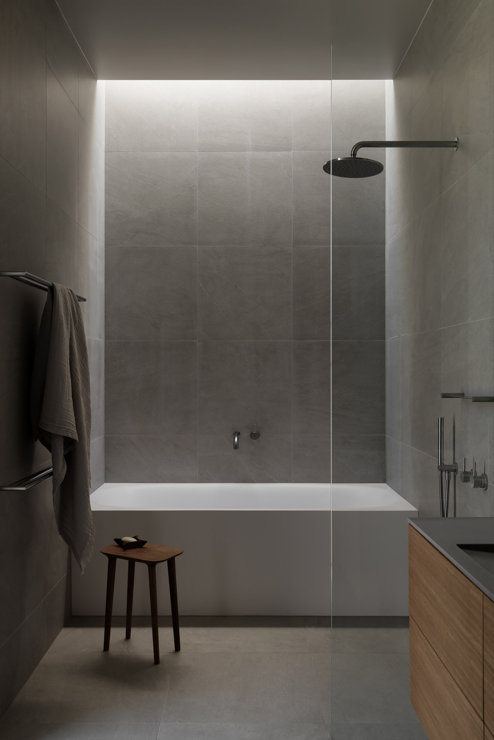 Bathroom with grey tile walls and concealed linear lighting above the bathtub alcove