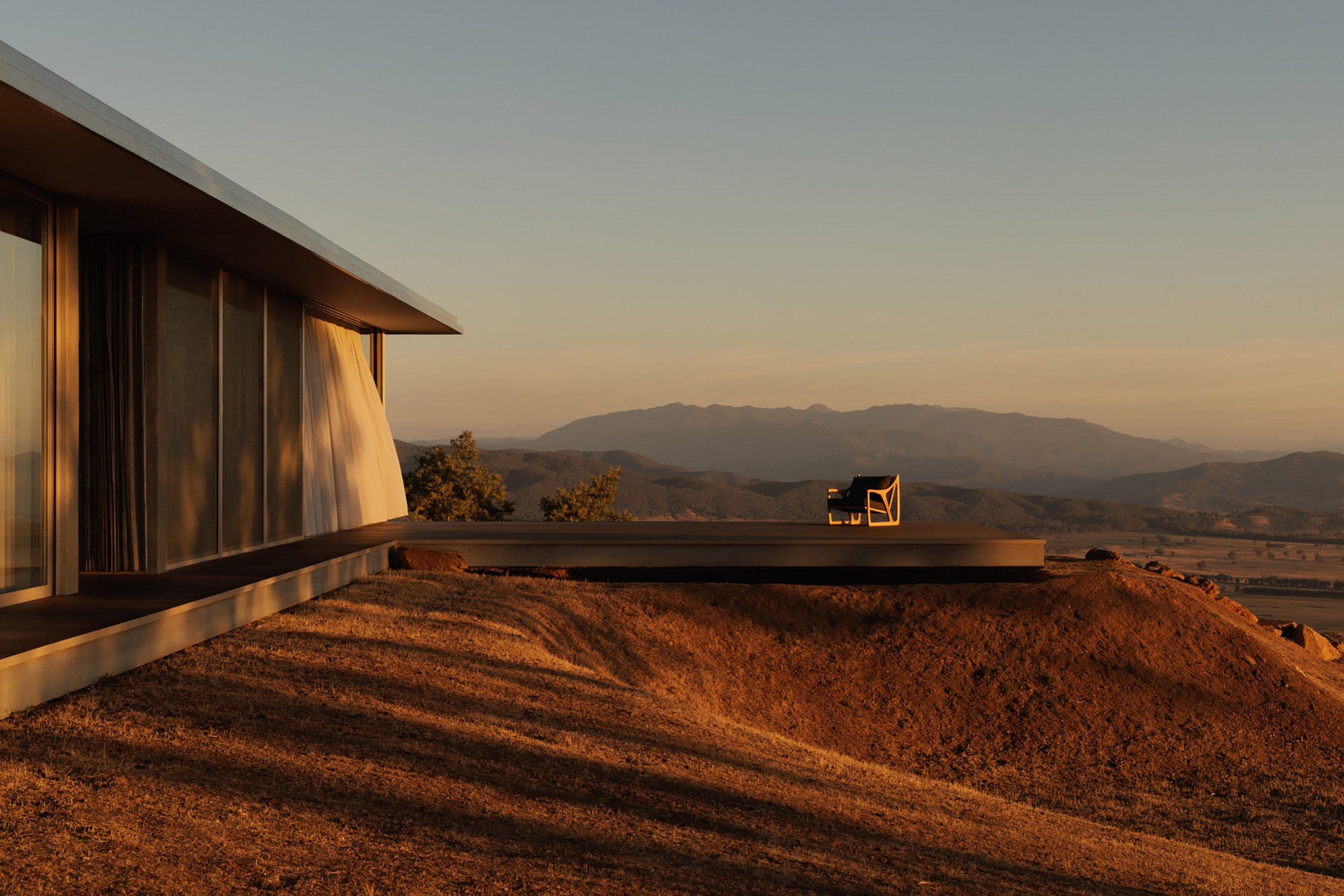 Cantilevered terrace perched above excavated hillside with mountain range visible at dusk