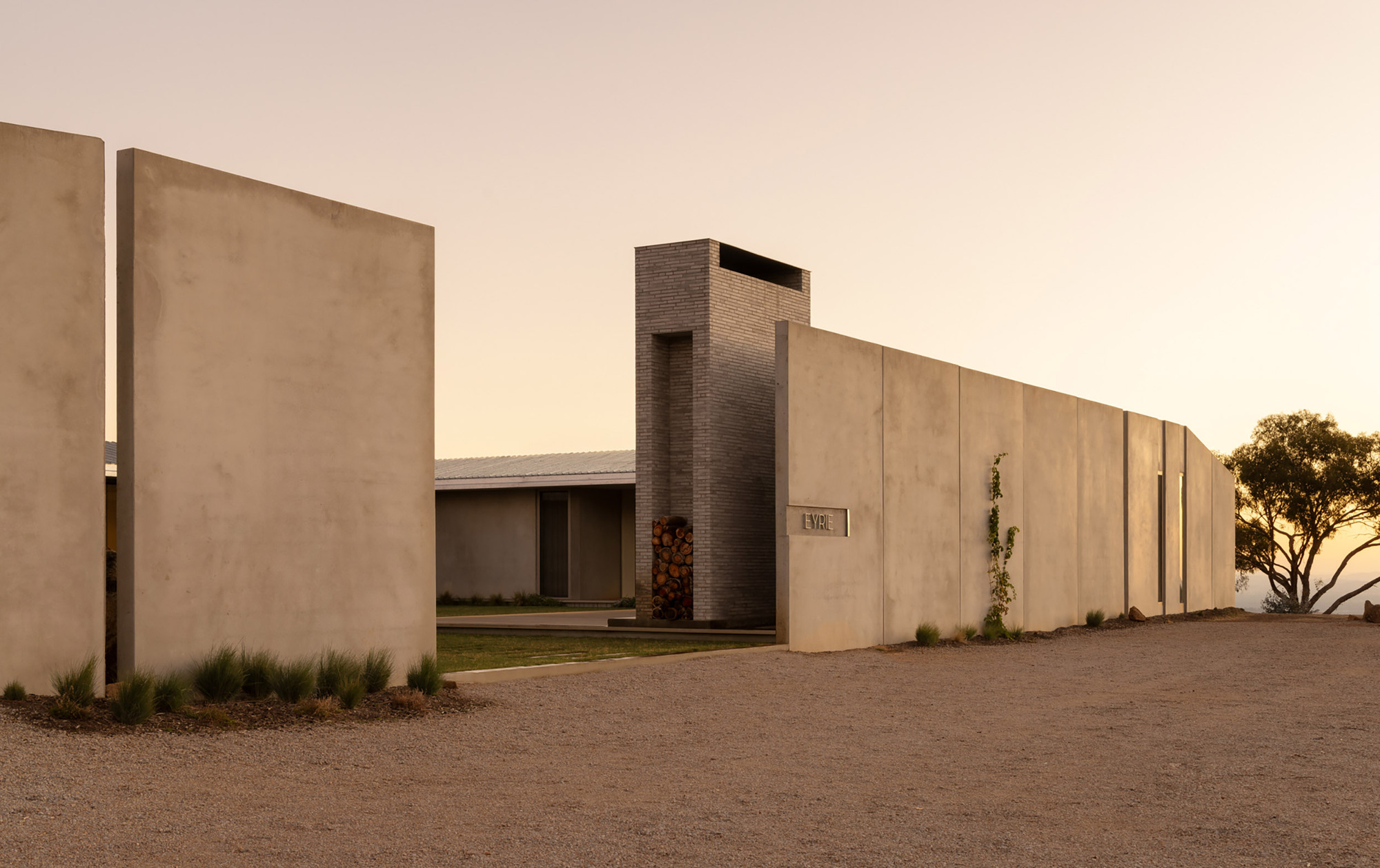 Street view of paneled concrete perimeter wall with brick chimney tower at golden hour