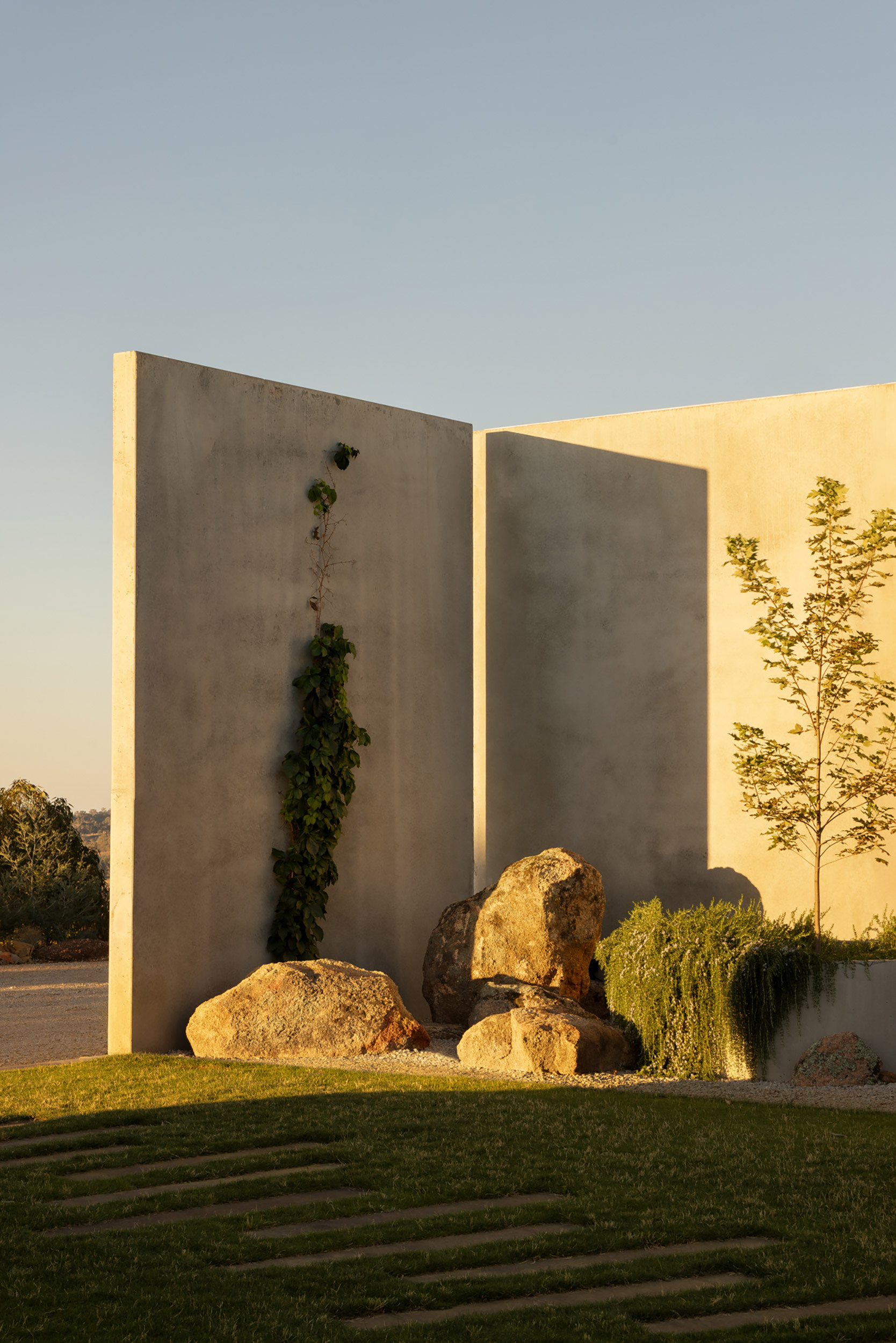 Concrete entry walls with recessed lighting flanking boulders and plantings at sunset
