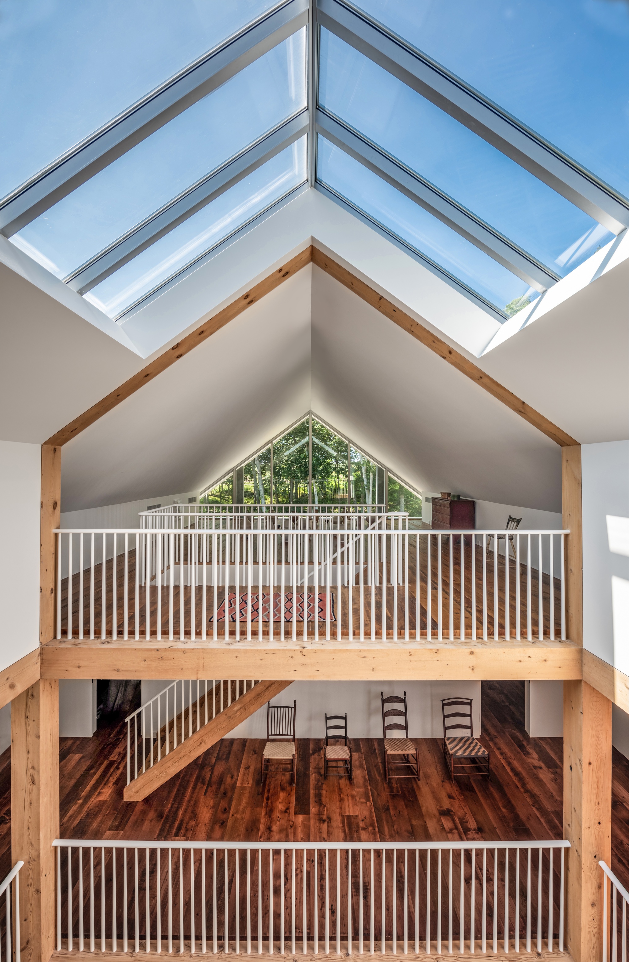 Interior view of double-height space with exposed timber frame, vertical railing balconies, and ridge skylight