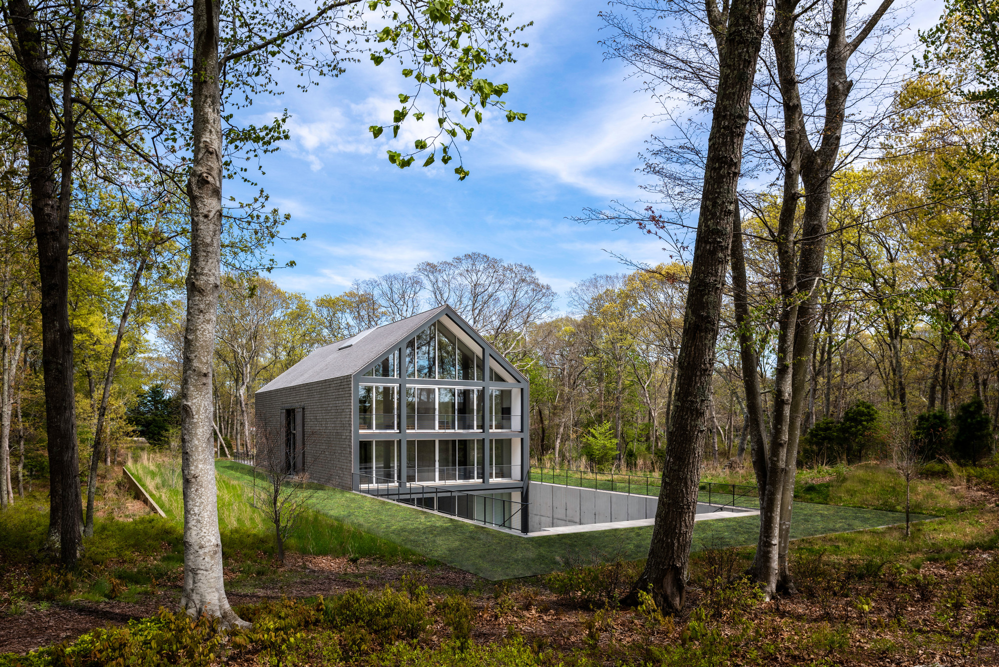 Glass gable end elevation seen through bare autumn trees with gravel terrace below