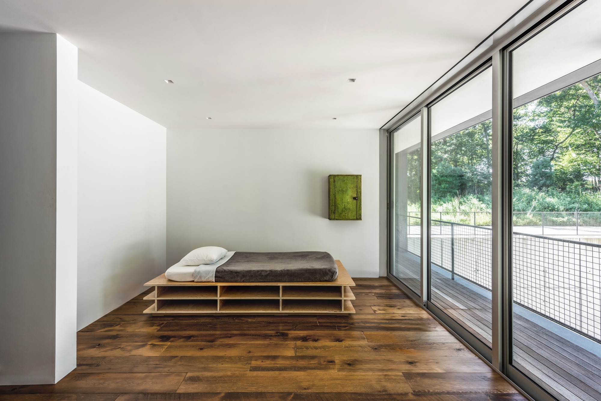 Minimalist bedroom with low platform bed on dark wood flooring and full-height glazed doors opening to a terrace