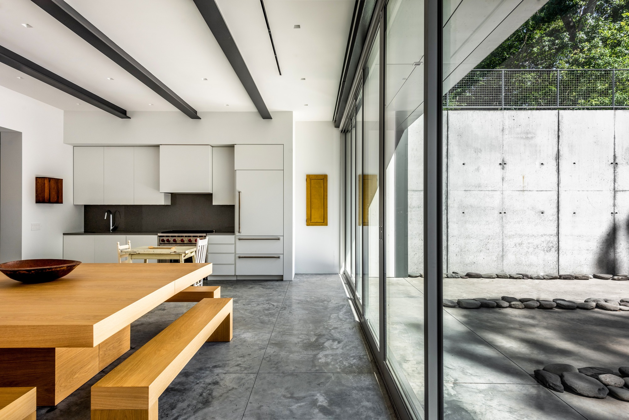 Kitchen with light cabinetry and sliding glass doors looking onto a concrete courtyard with dappled shadows
