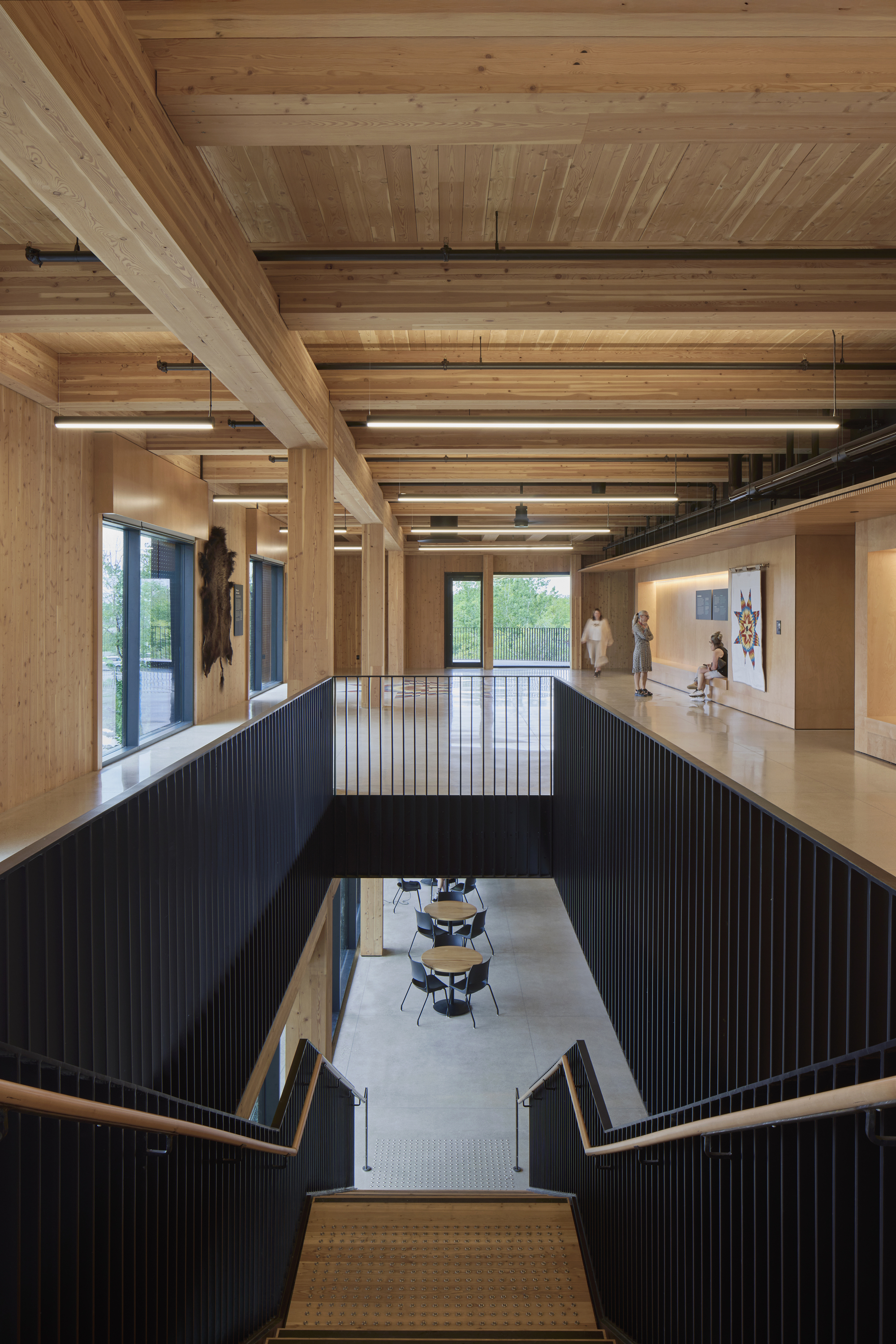 Two-story interior atrium with exposed timber ceiling beams and black vertical railing around central void
