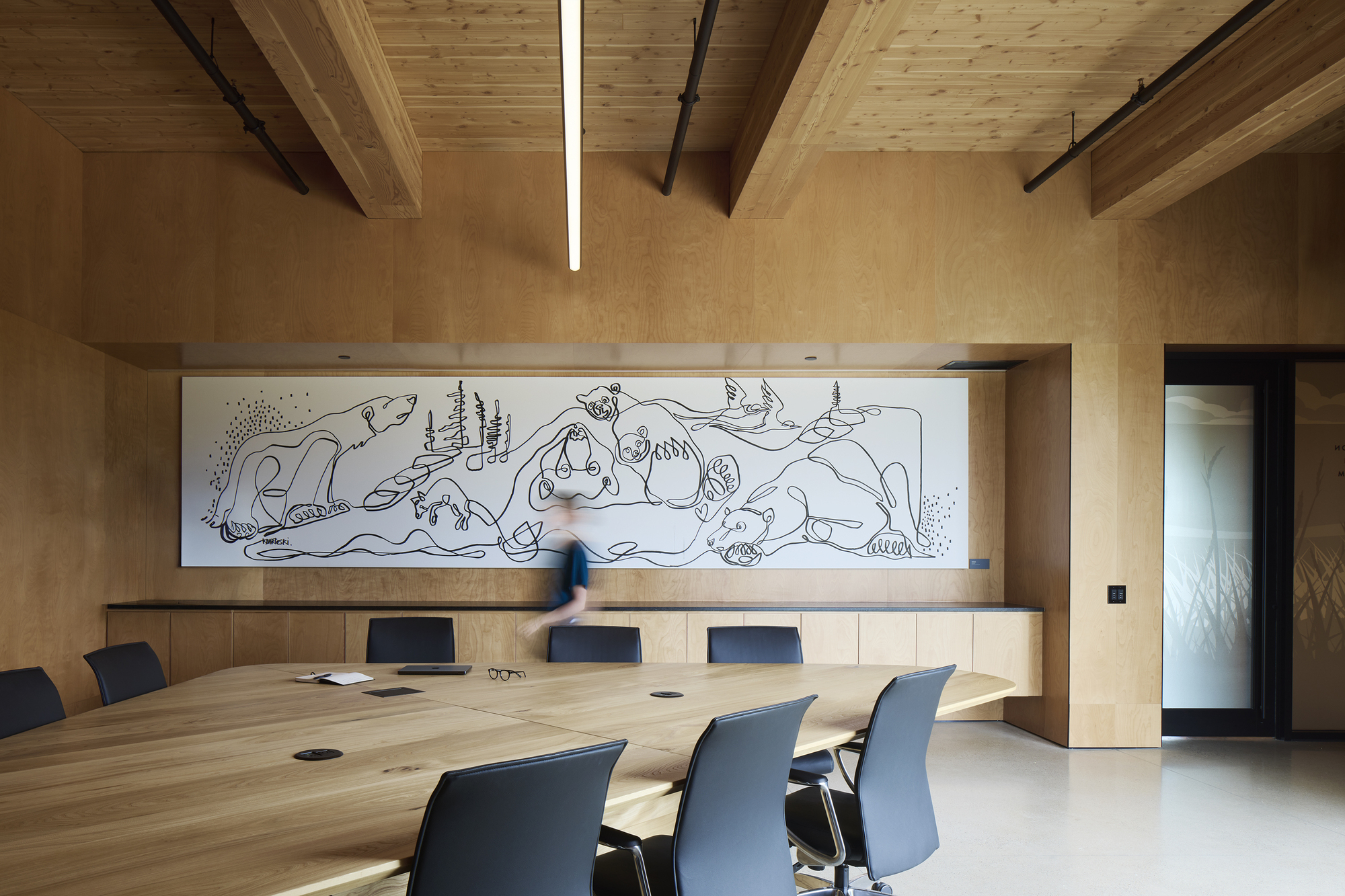 Conference room with long timber table and wall mural under exposed beam ceiling with linear lighting