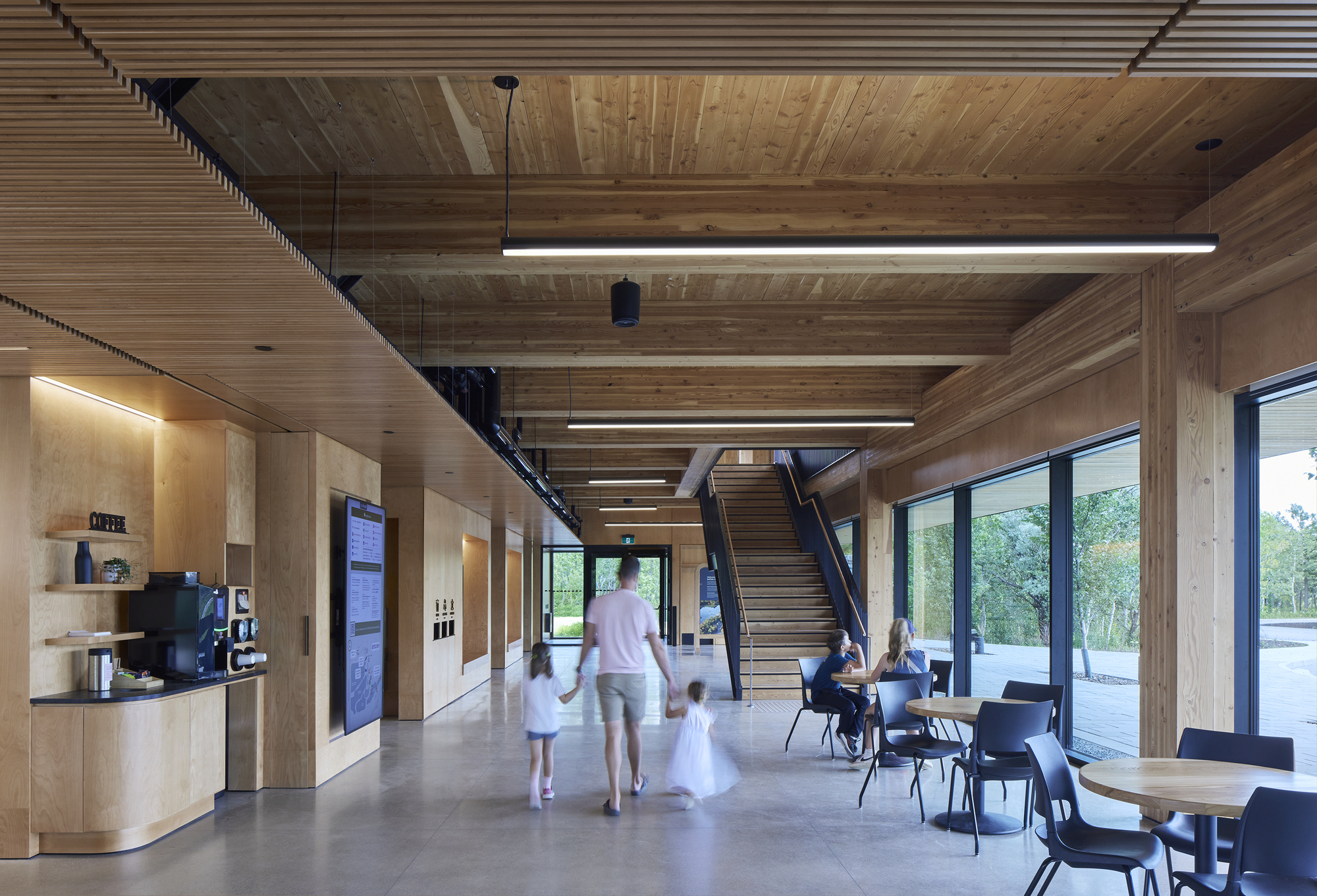 Lobby with exposed timber ceiling beams, steel staircase, and family walking through the space