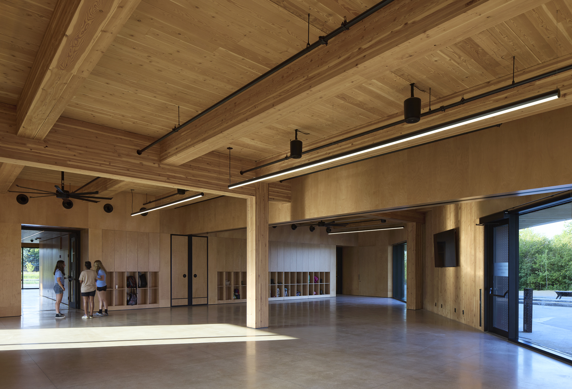 Interior view of open room with timber ceiling, plywood walls, and visitors near sunlit glazing