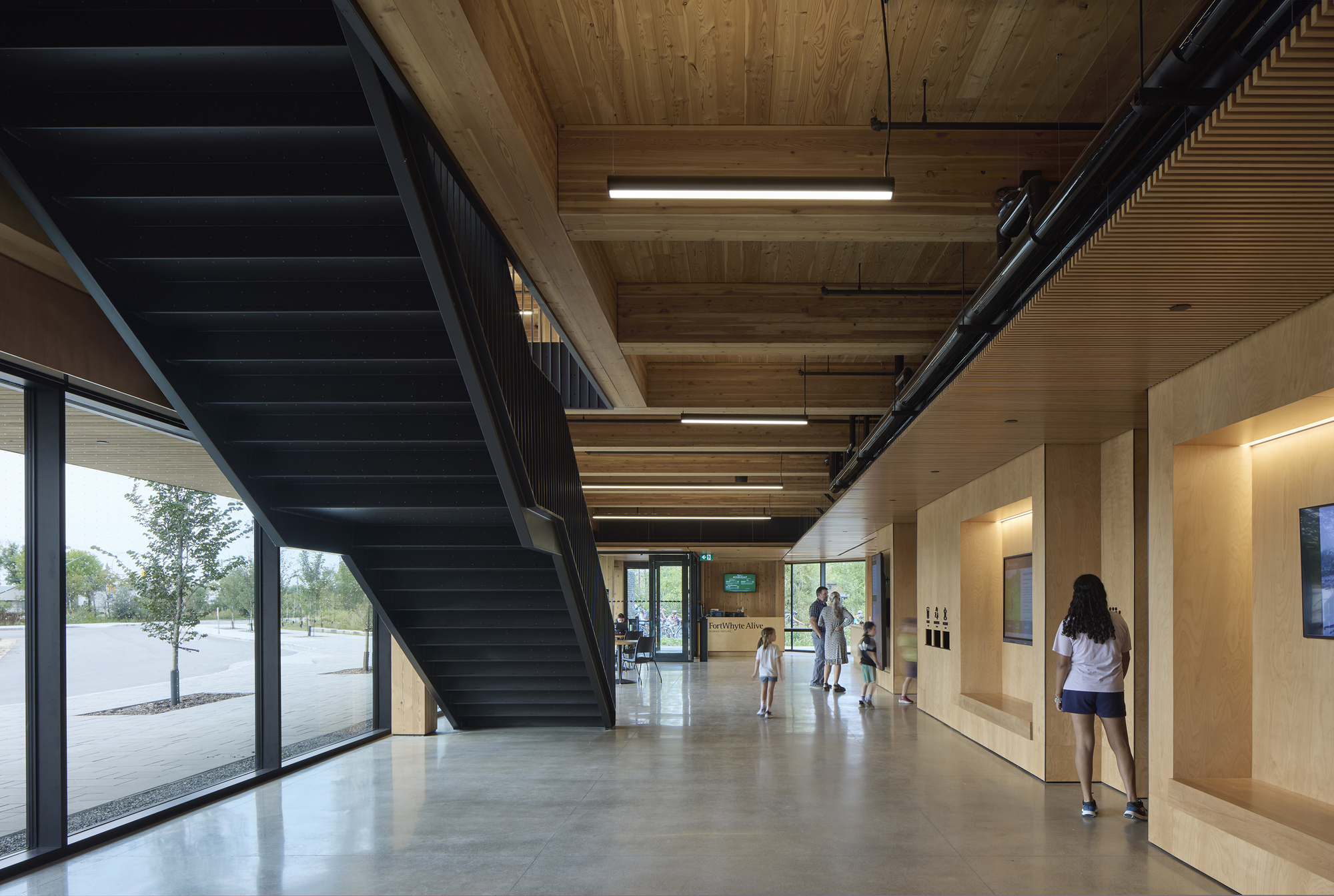 Main circulation corridor with blackened steel staircase ascending beneath exposed timber ceiling structure
