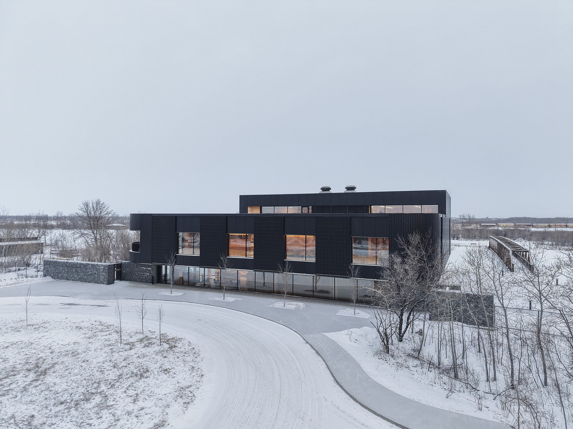 Aerial view showing the black corrugated envelope and curved access drive in a snowy landscape