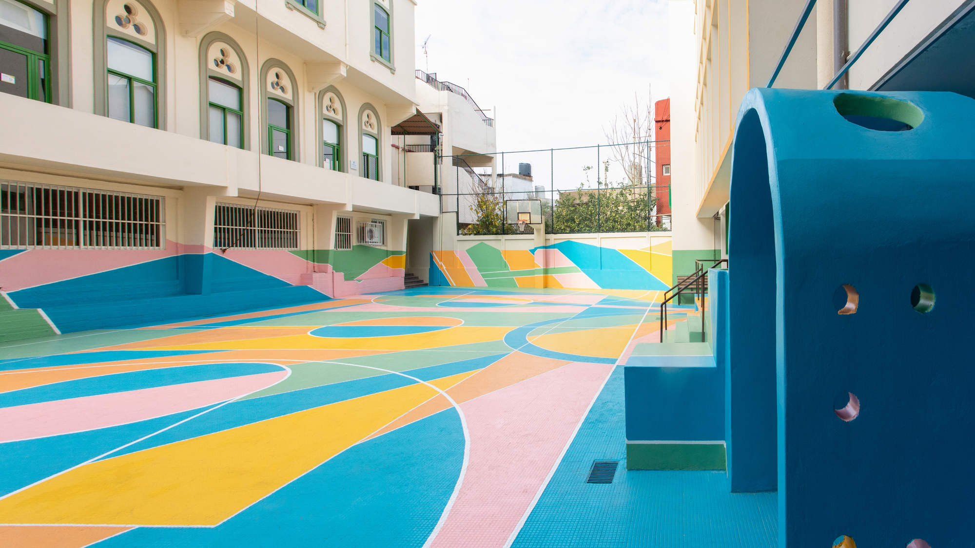 Exterior courtyard with multicolored geometric patterning across the sport court surface and blue climbing structure