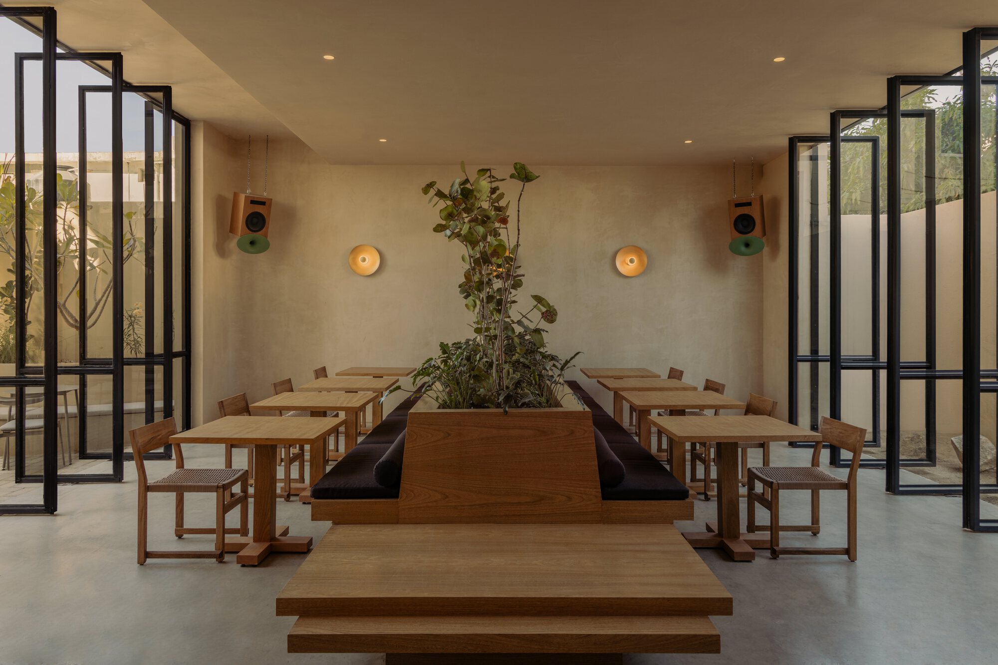 Interior dining room with timber tables flanking a central planter and steel-framed glass doors
