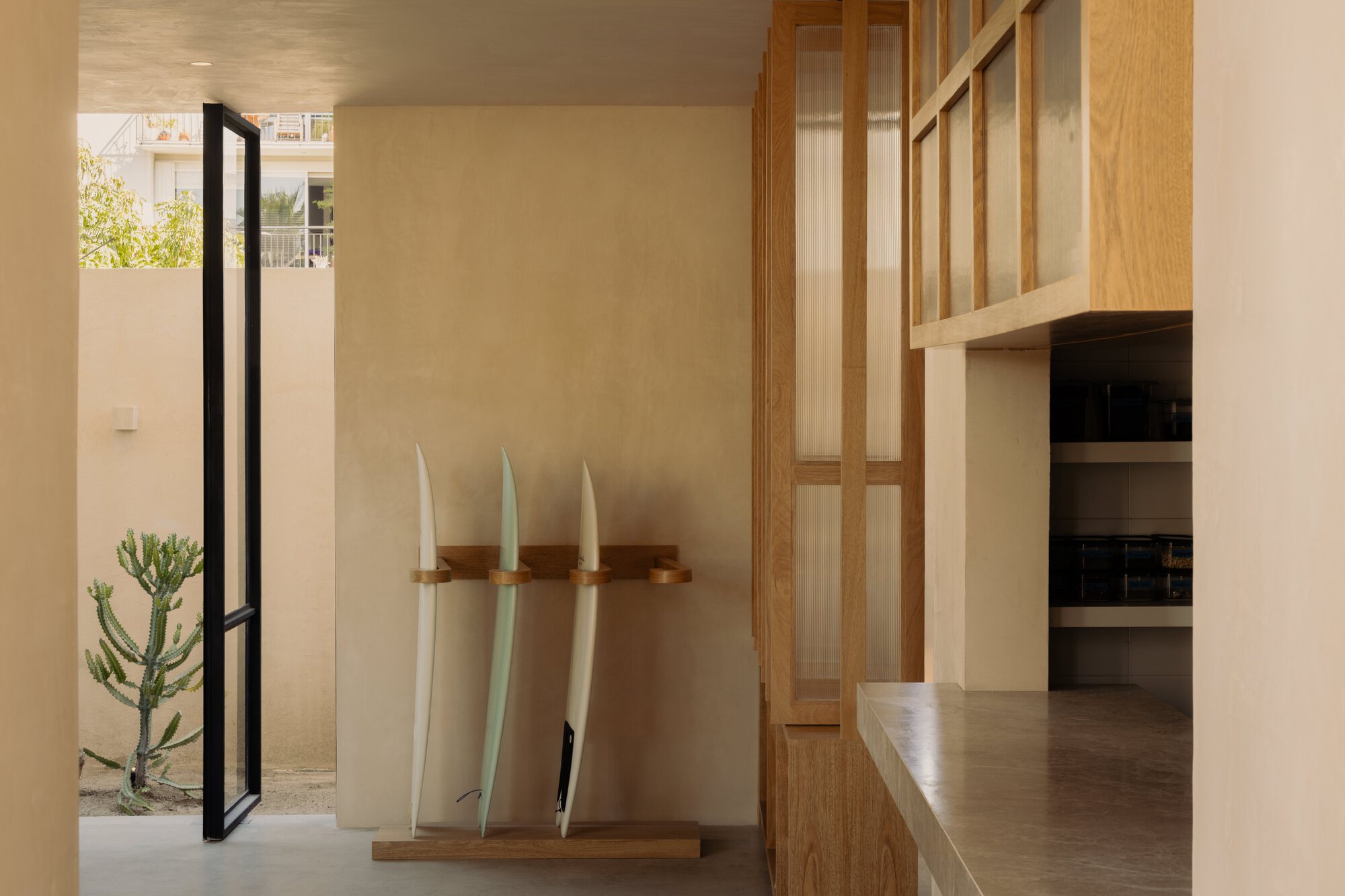 Entry foyer with timber screen and surfboard rack near a steel-framed door to the courtyard