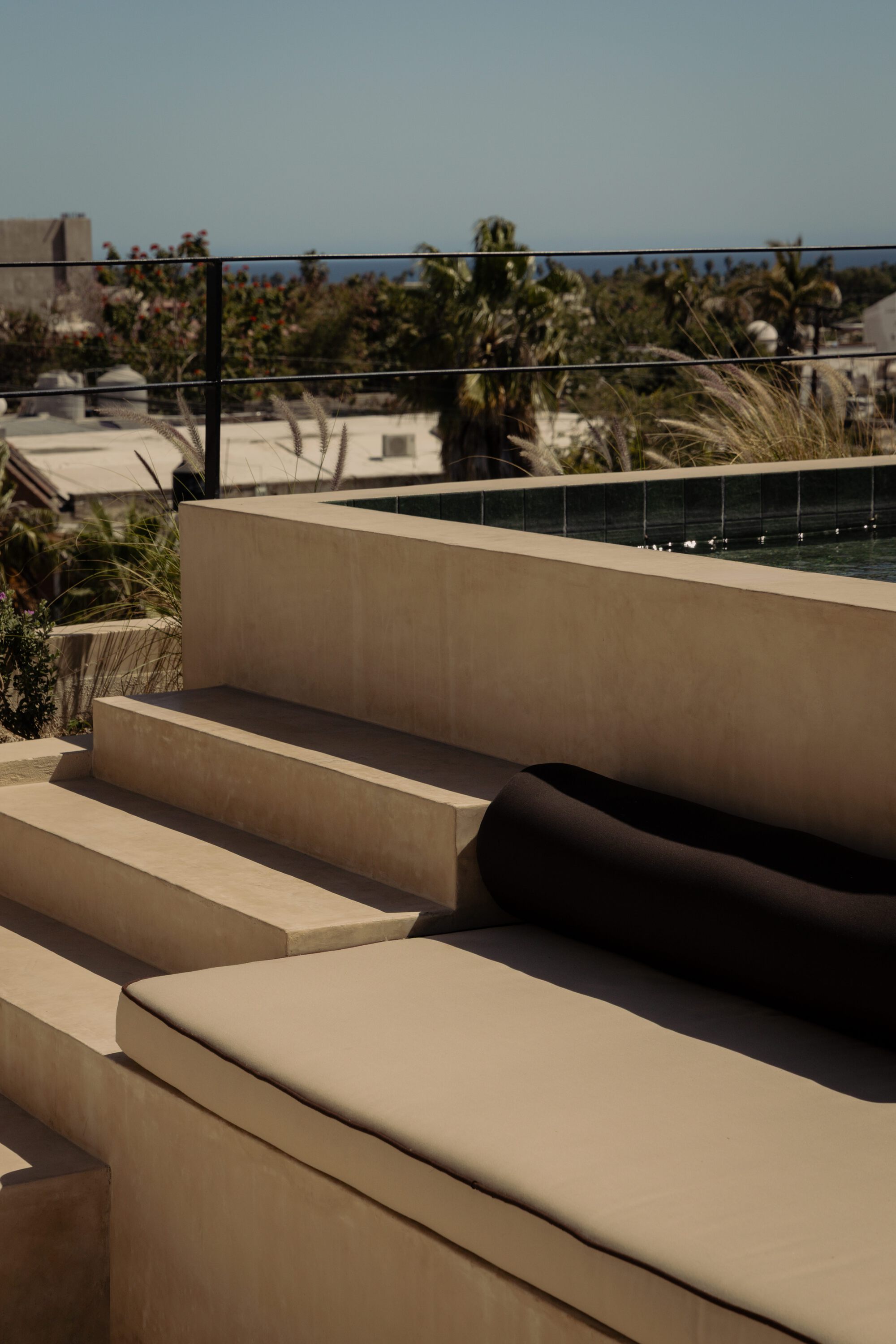 Built-in seating steps in stucco with cushions beside a glass-railed pool deck