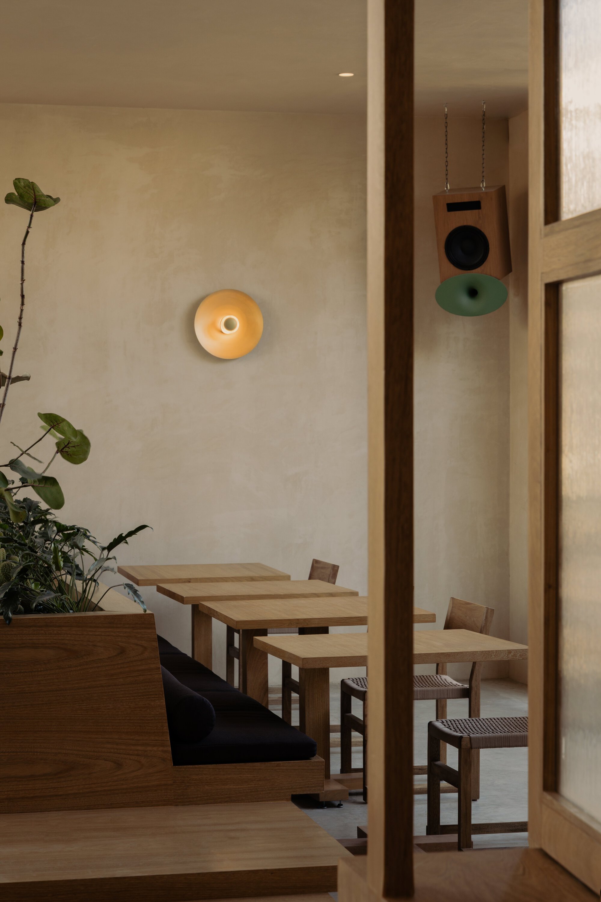 Timber dining tables and chairs framed by wooden columns with wall sconce in evening light
