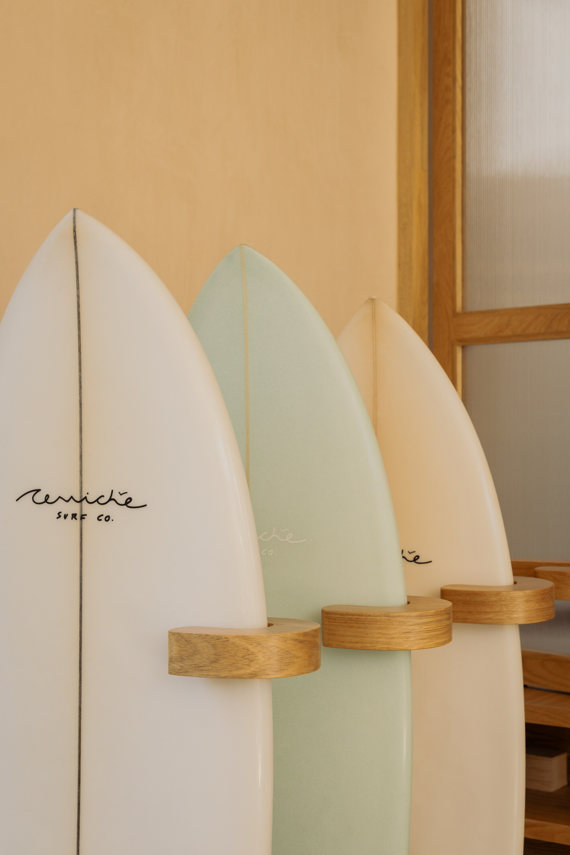 Three surfboards mounted on wooden pegs against a pale plywood wall and glass partition