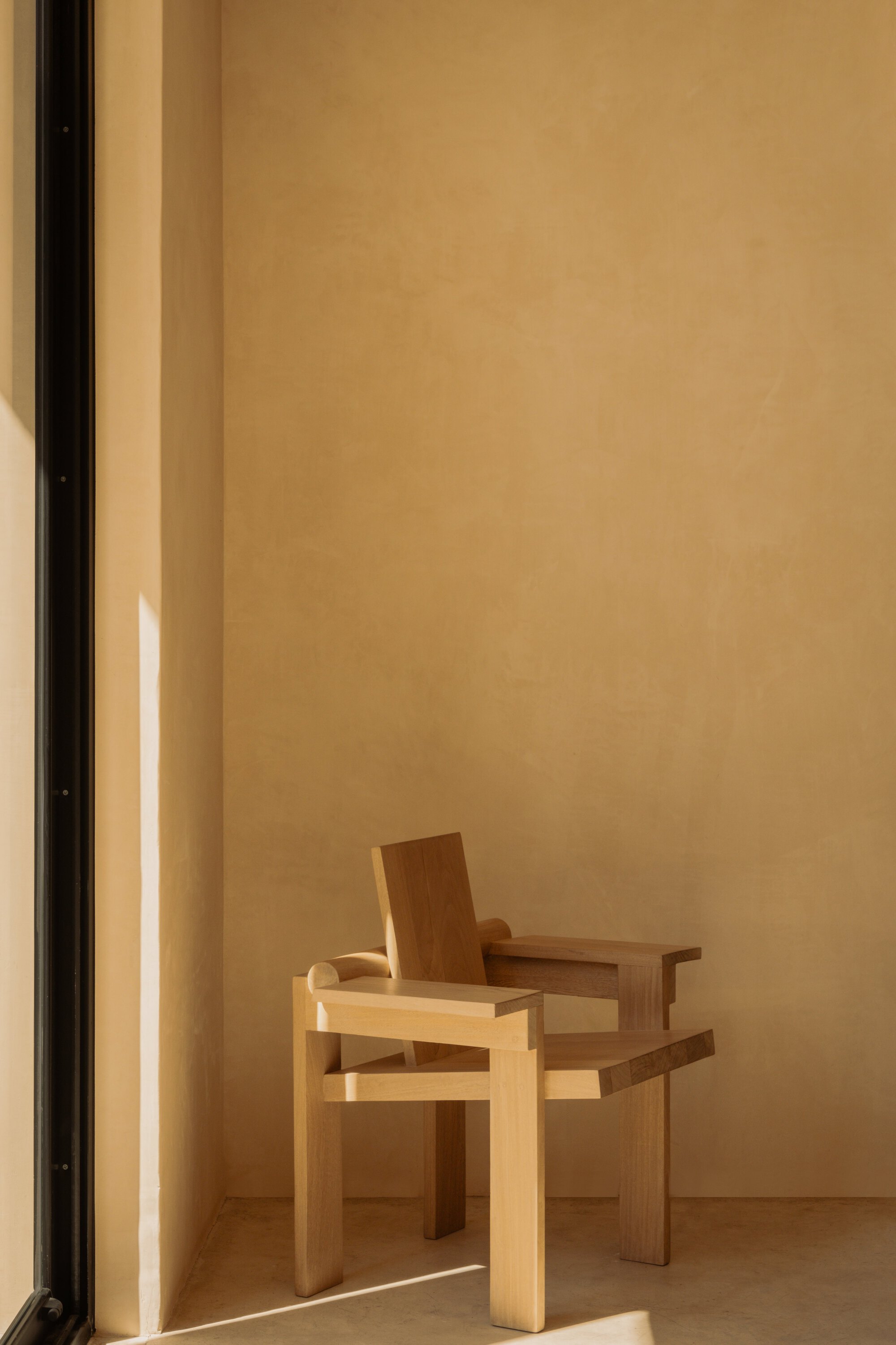 Two timber chairs sit in a sunlit room with pale wood flooring and smooth plaster walls