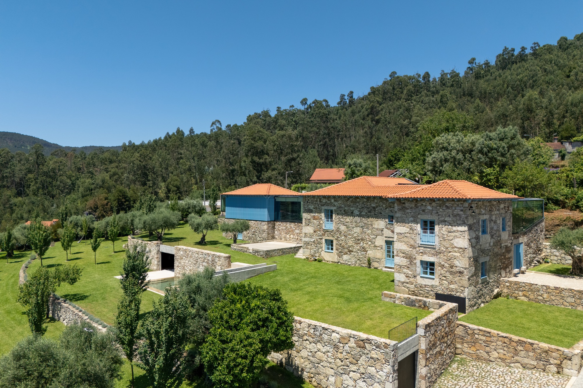 Stone farmhouse with terracotta tile roofs and blue shutters set among terraced lawns and olive trees