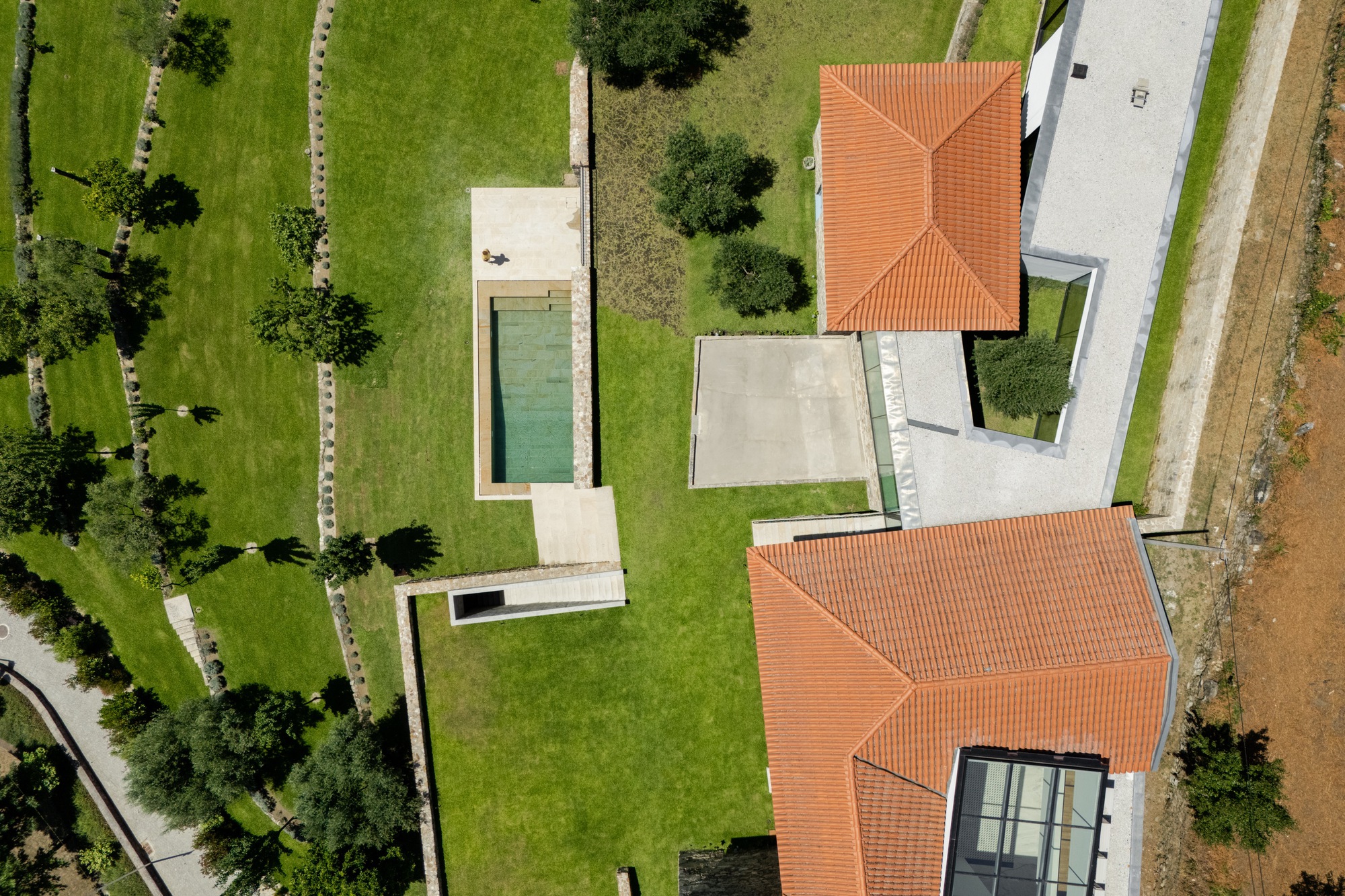 Aerial view showing terracotta hip roofs, swimming pool and white courtyard terraces among planted lawns