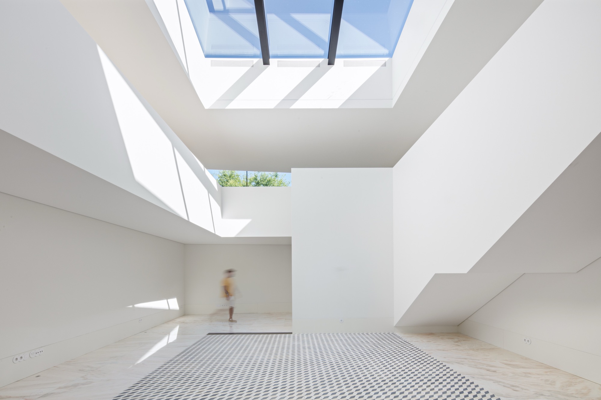 Double-height interior space with skylights, metal floor grating and a figure passing through sunlit openings