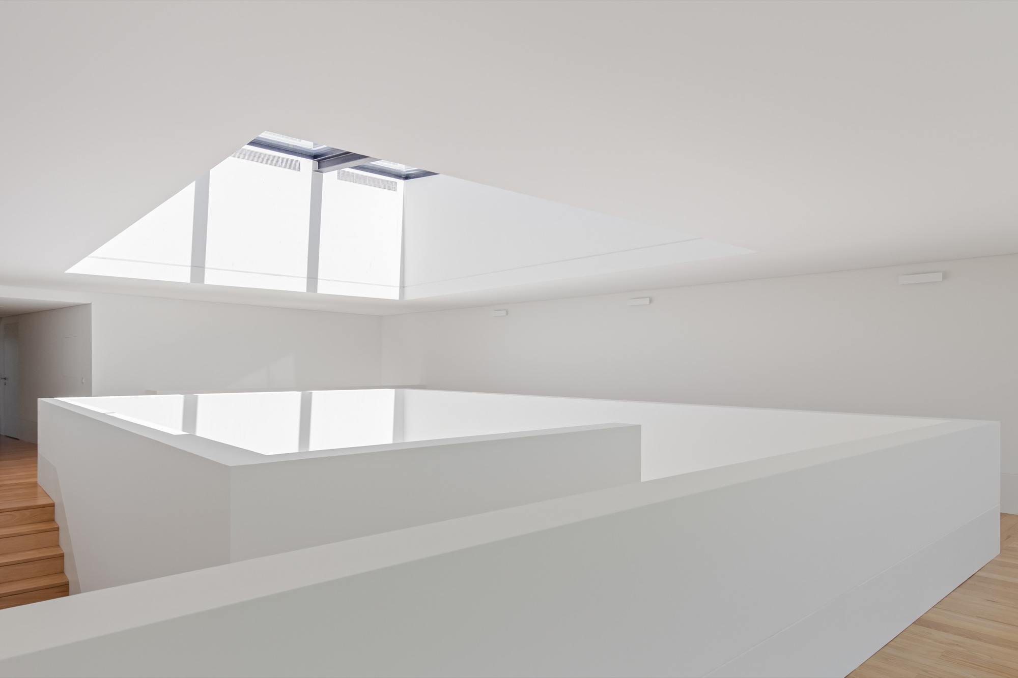 White parapet walls defining an upper level void beneath an open skylight with timber flooring beyond