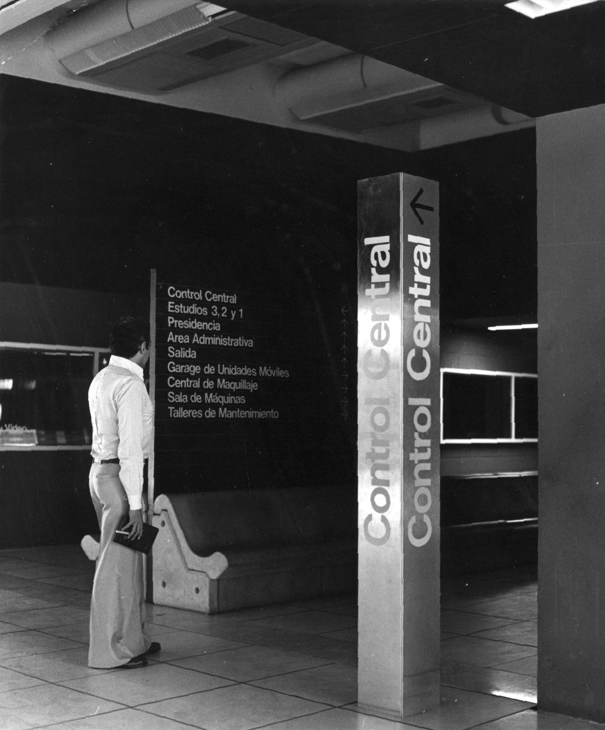 Interior lobby with freestanding directional signage column and visitor carrying a briefcase