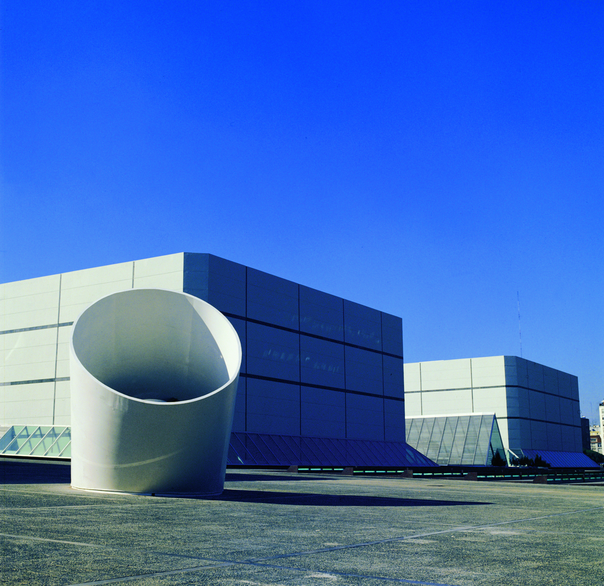 Blue and white paneled facade with large cylindrical volume under a clear sky