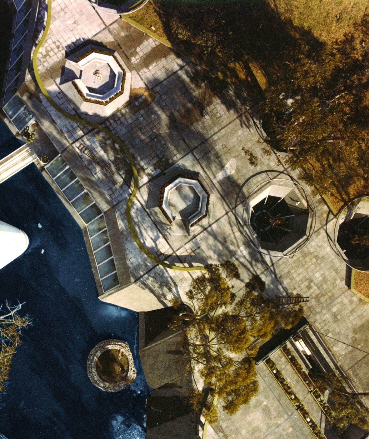 Overhead view of paved plaza with octagonal pavillions and tree shadows in afternoon light