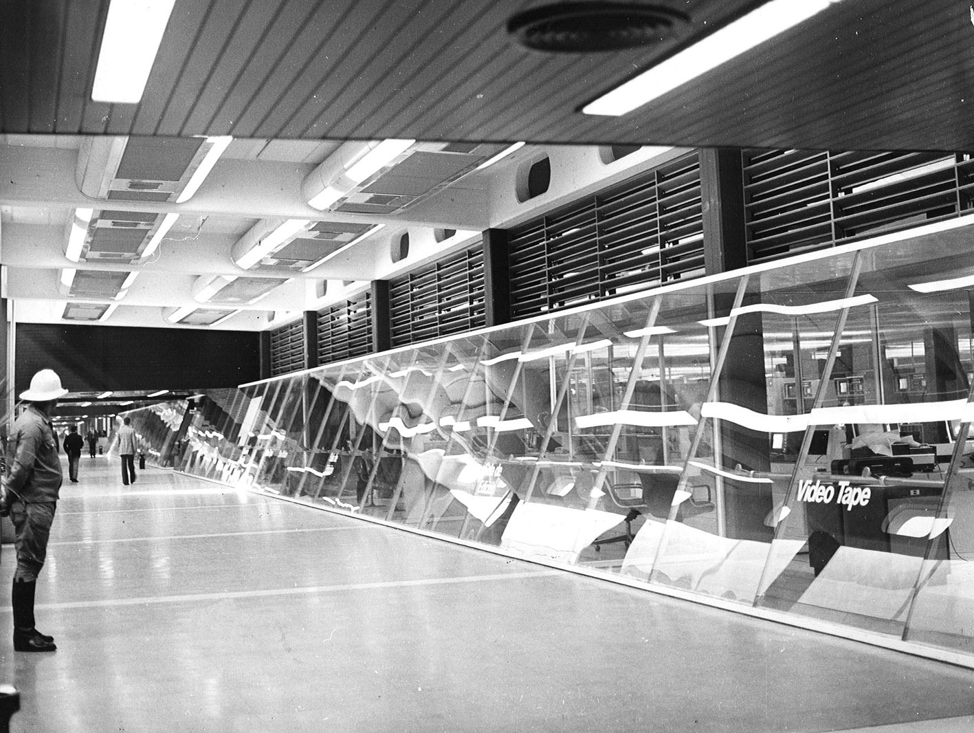 Interior hall with angled white structural frames and overhead arrival departure boards with visitors walking