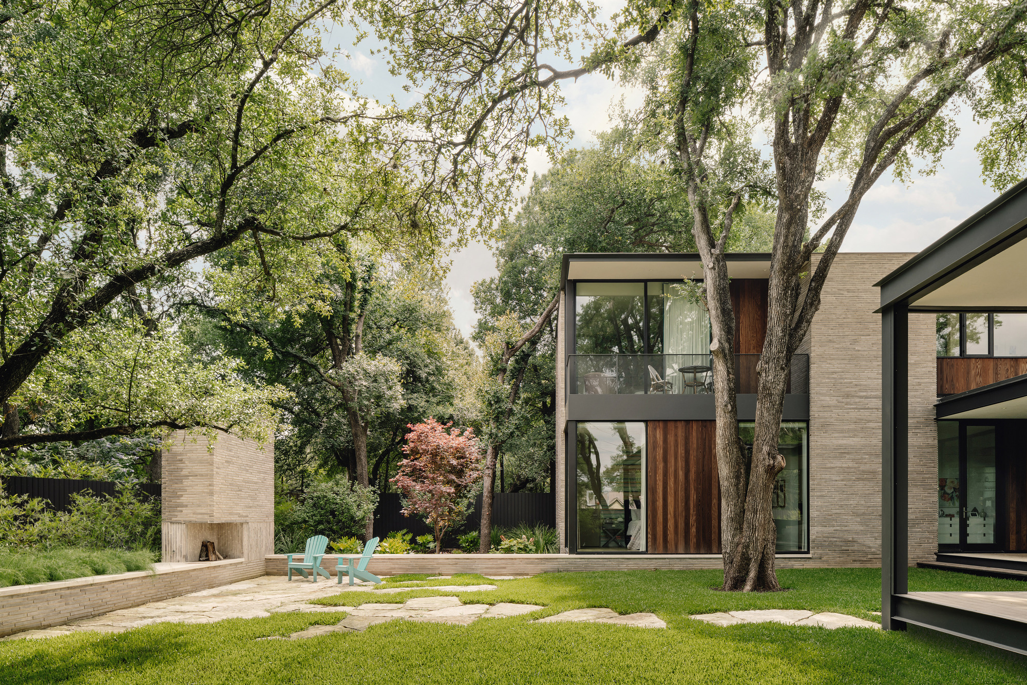 Rear courtyard showing the two-story glazed volume with timber cladding and outdoor fireplace