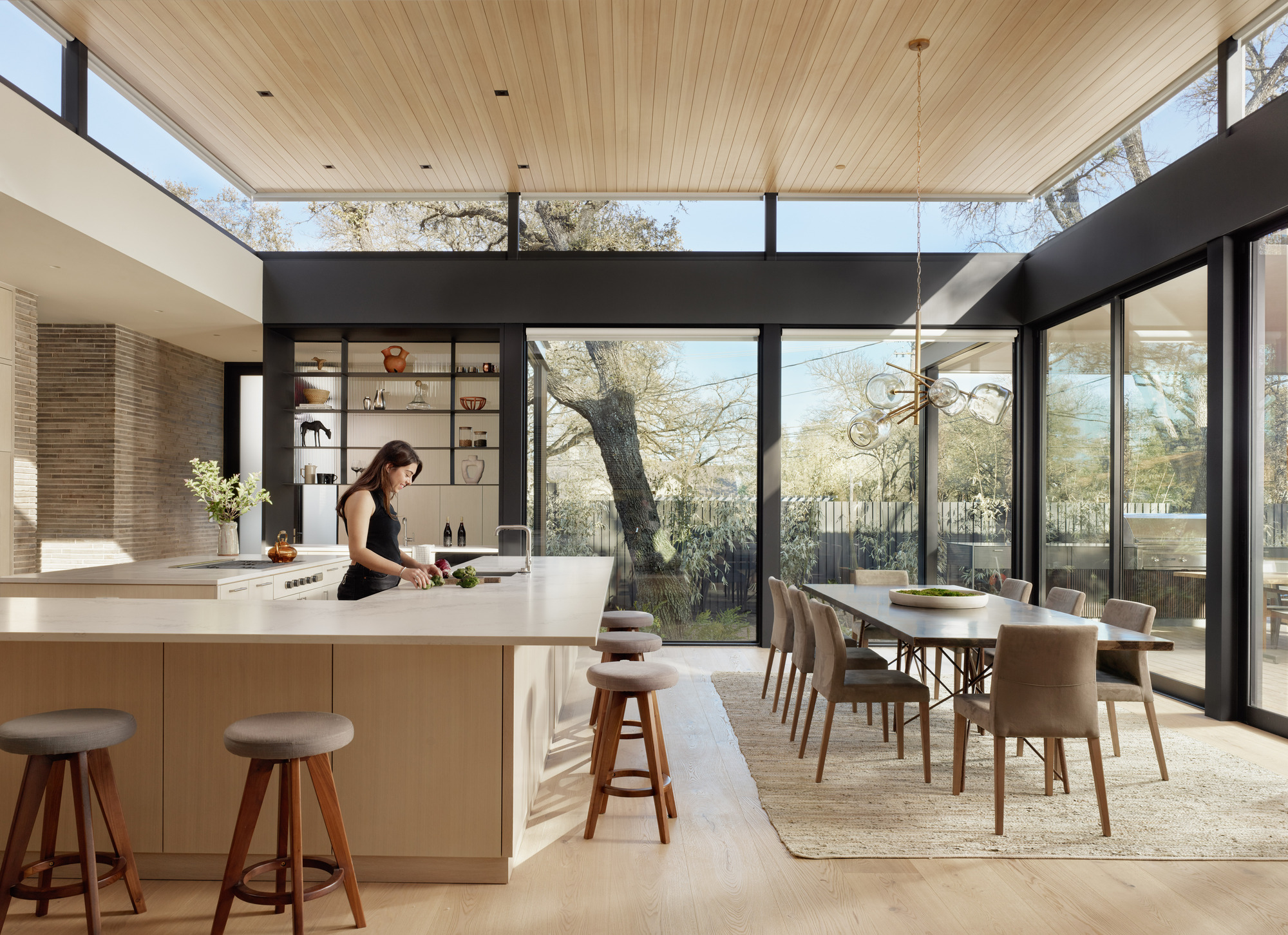 Open kitchen and dining area with wood slat ceiling and floor-to-ceiling windows facing the garden