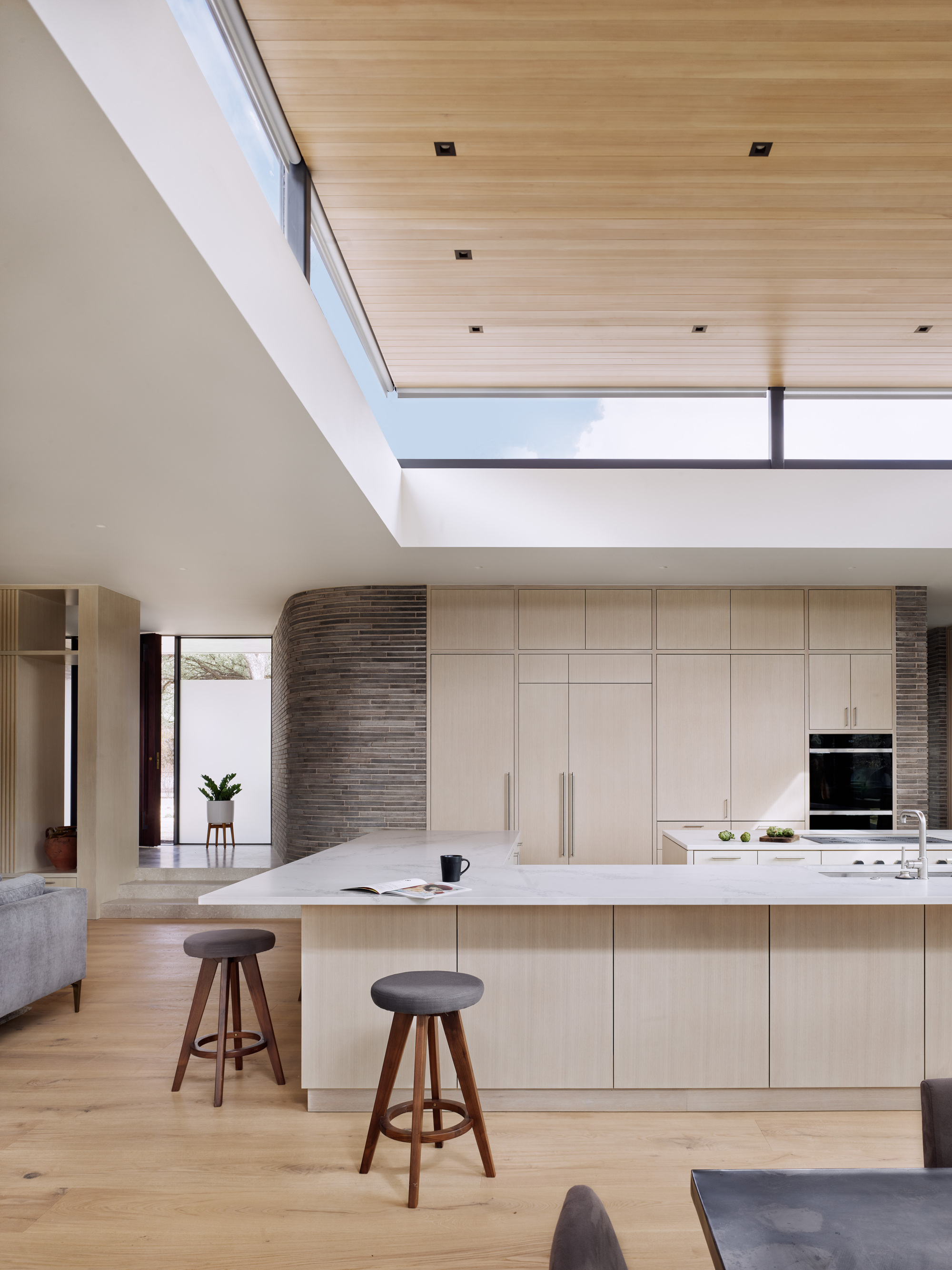 Kitchen island with pale cabinetry beneath a recessed wood ceiling and clerestory windows